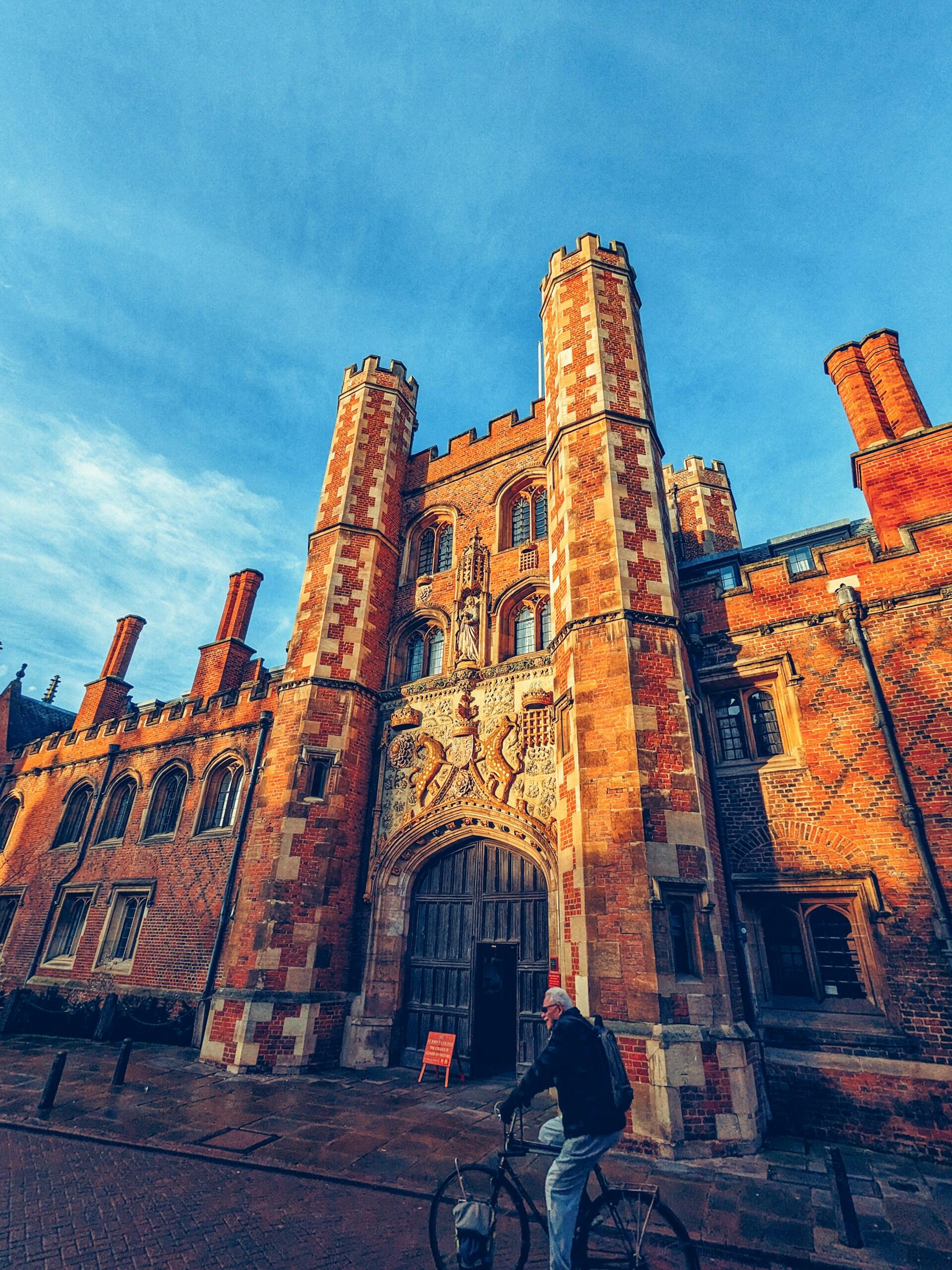 A man on a bicycle in front of a red brick building on a sunny day,