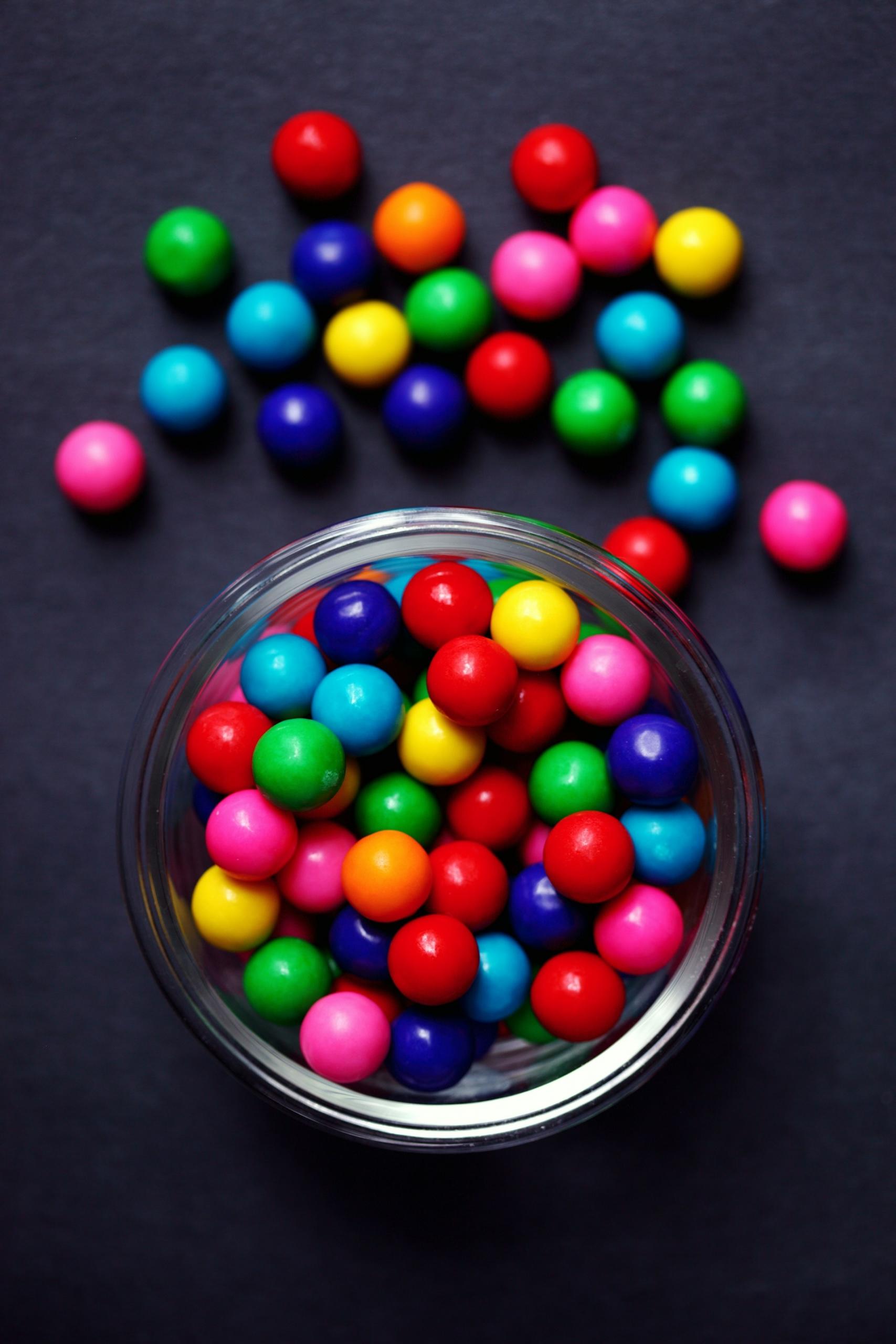 A bowl of sweets with some on the table outside the bow.