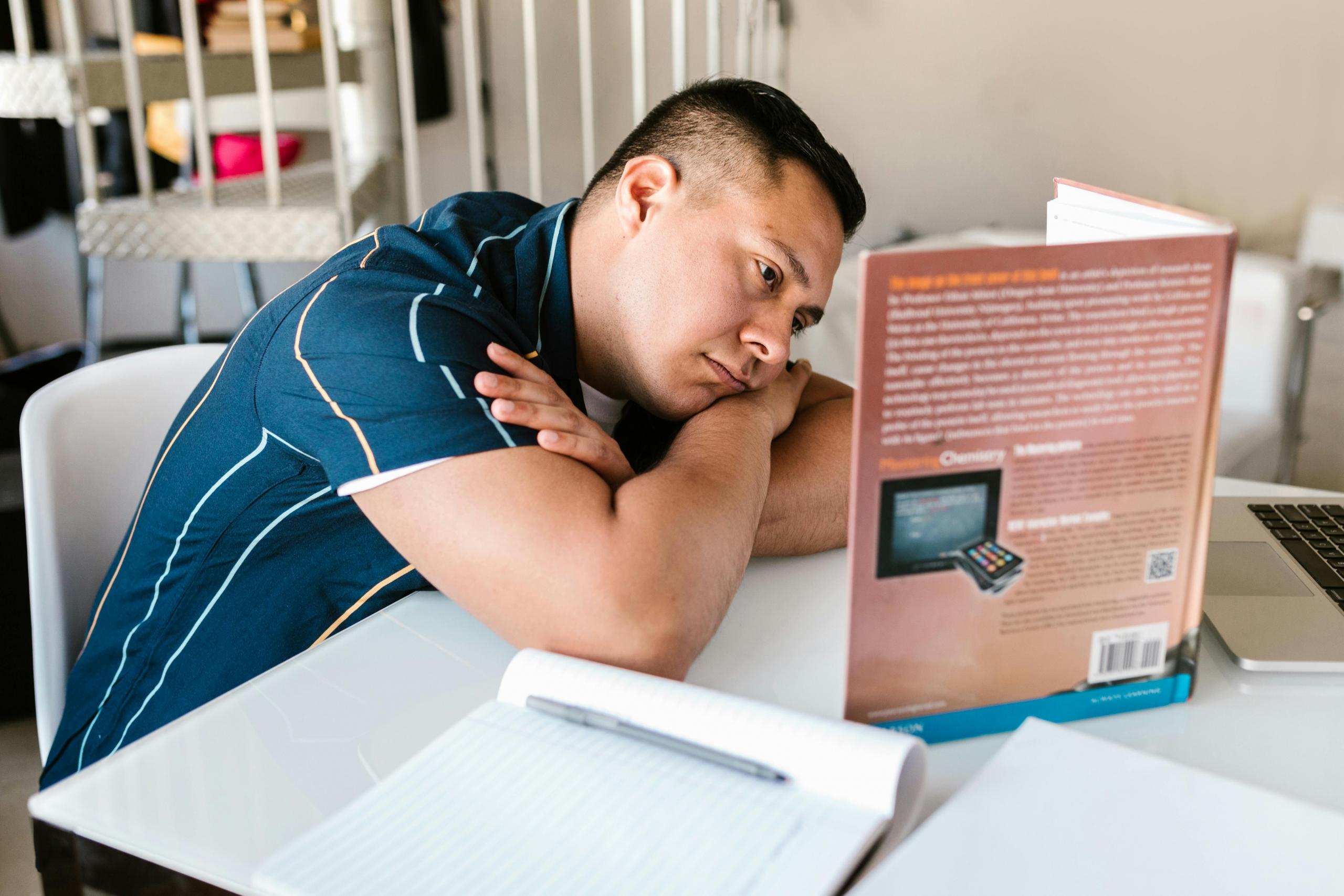 Man in a blue shirt sitting while reading a book on chemistry