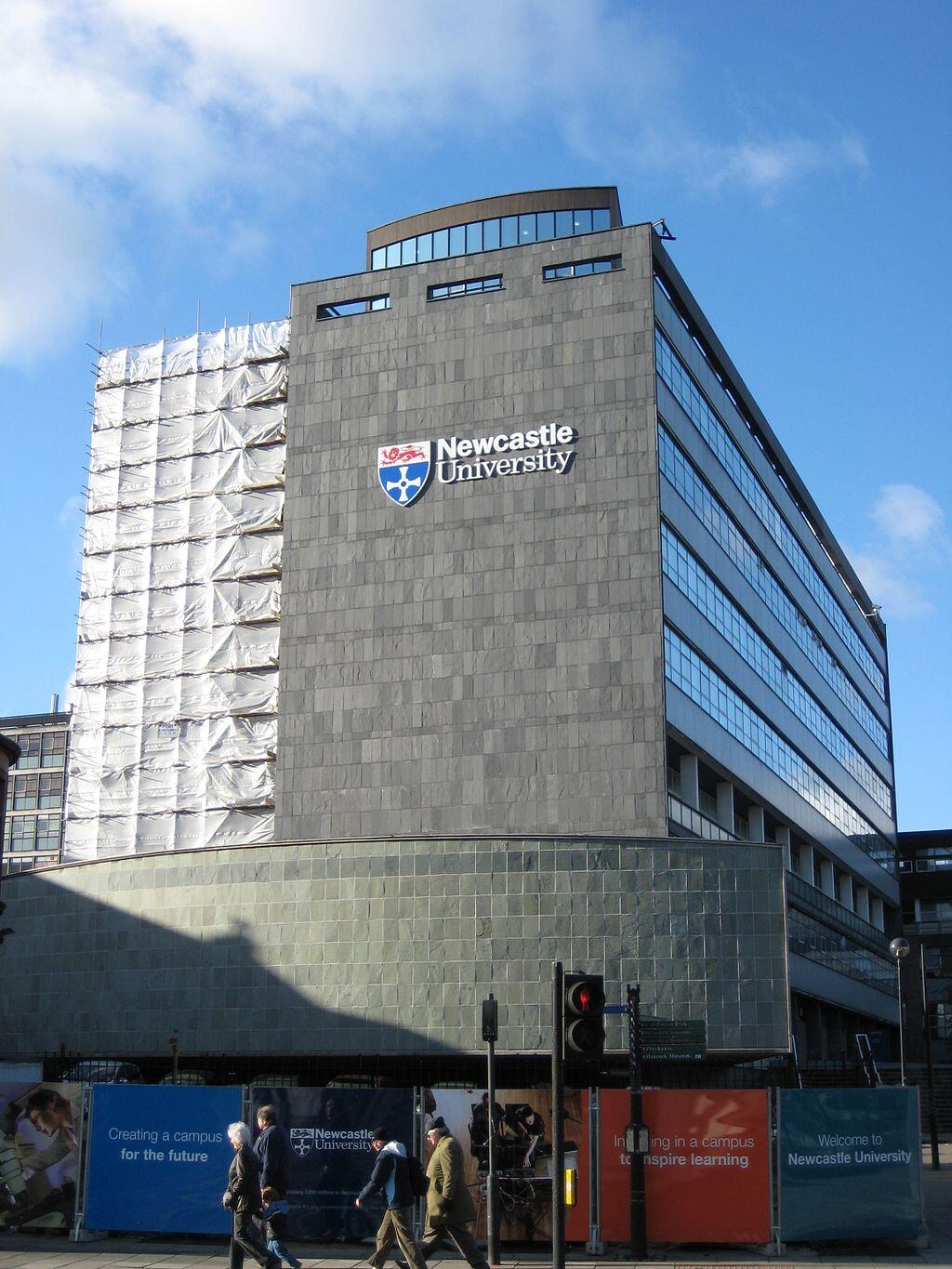 Newcastle University building facade with signage, pedestrians walking by, blue sky background.