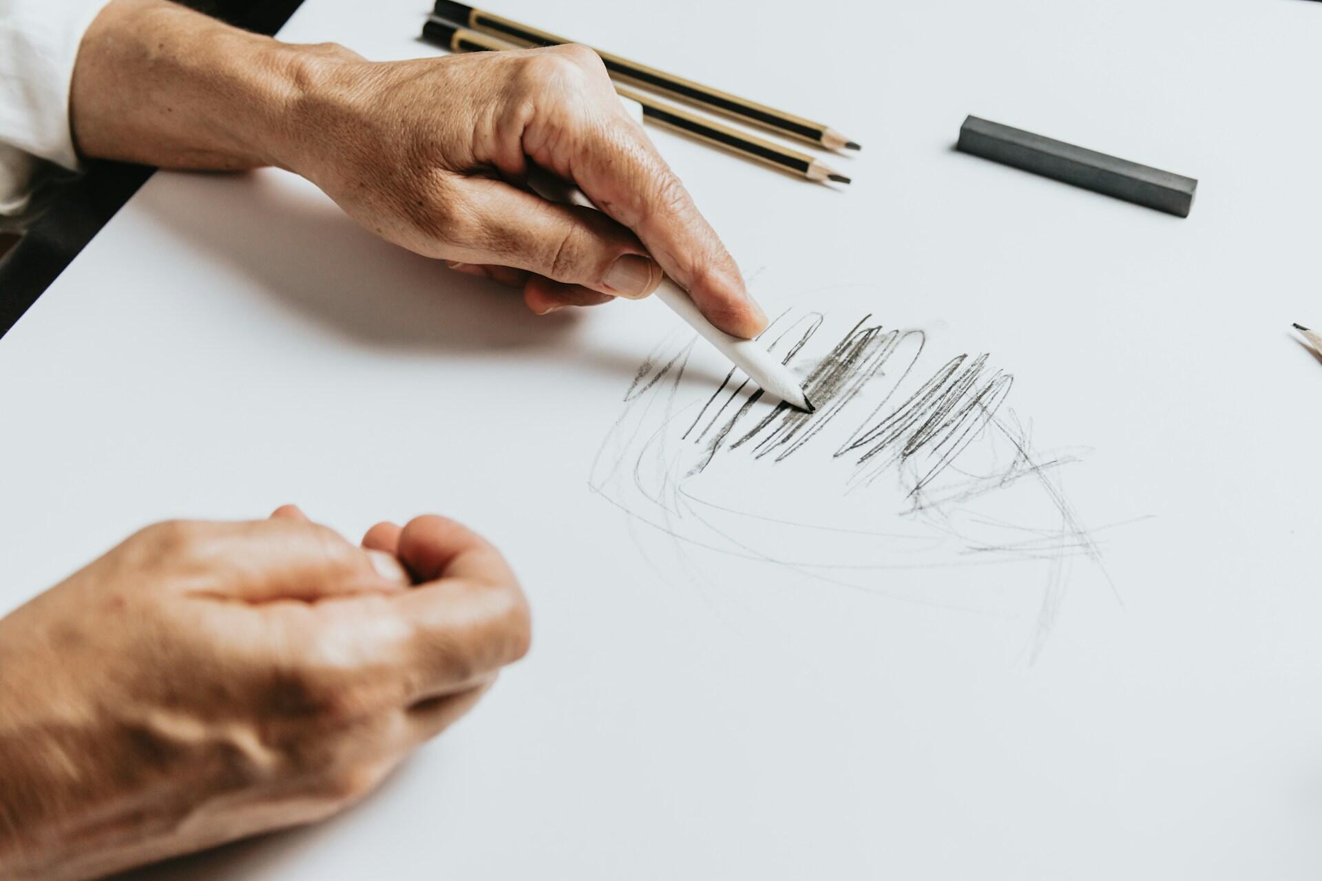 A person scribbling with a pencil on a white sheet of paper.