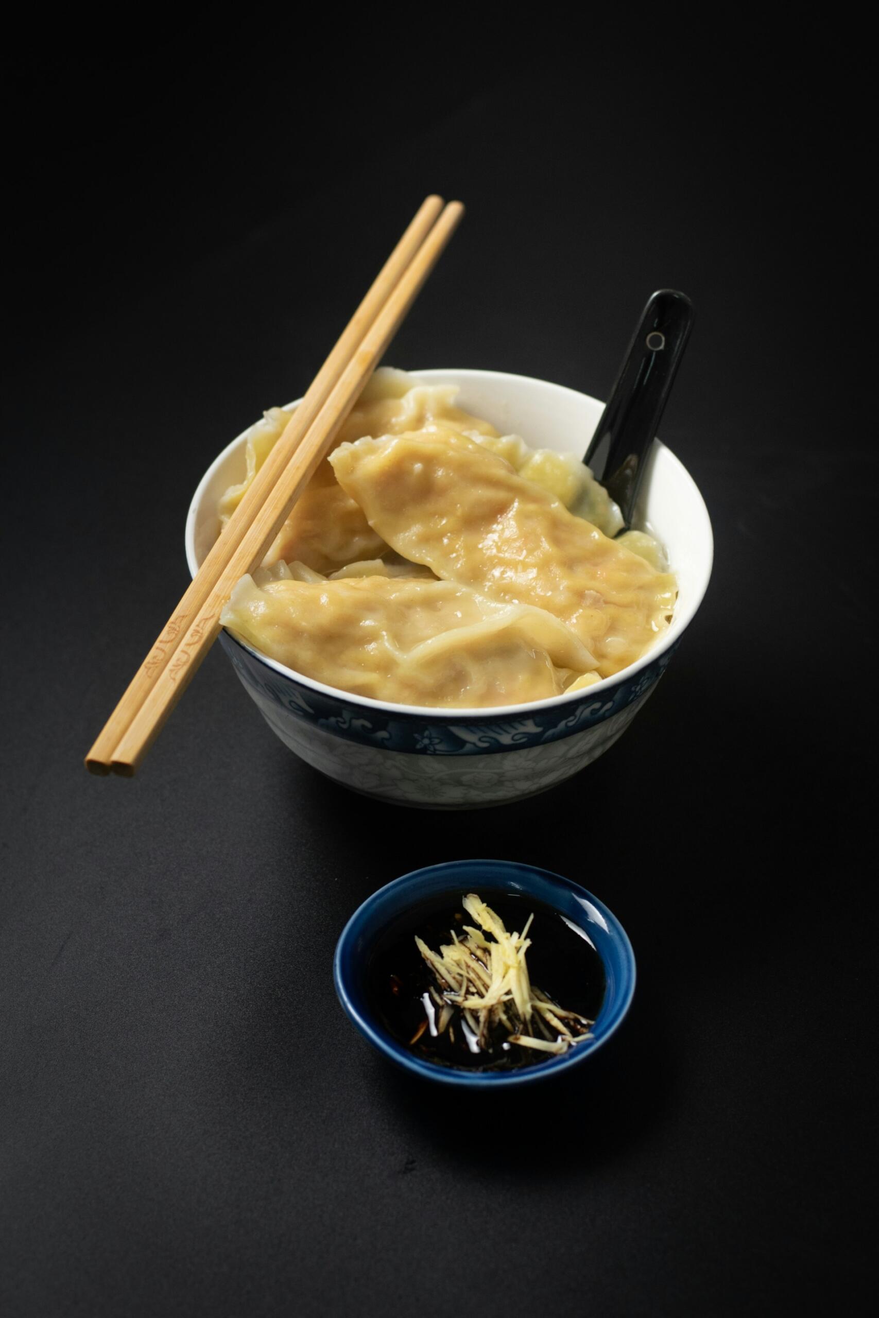 A bowl of Chinese dumplings with chopsticks and dipping sauce.