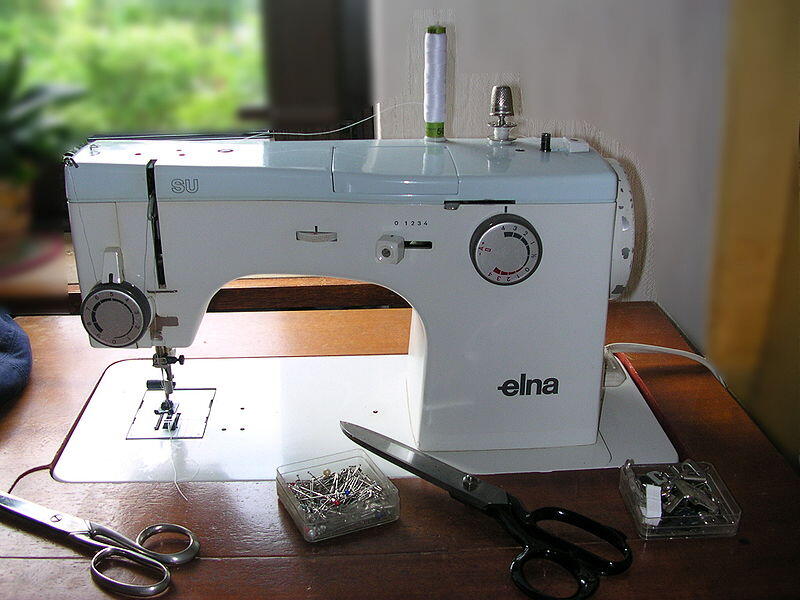 A flatbed sewing machine with sewing tools on a wooden table