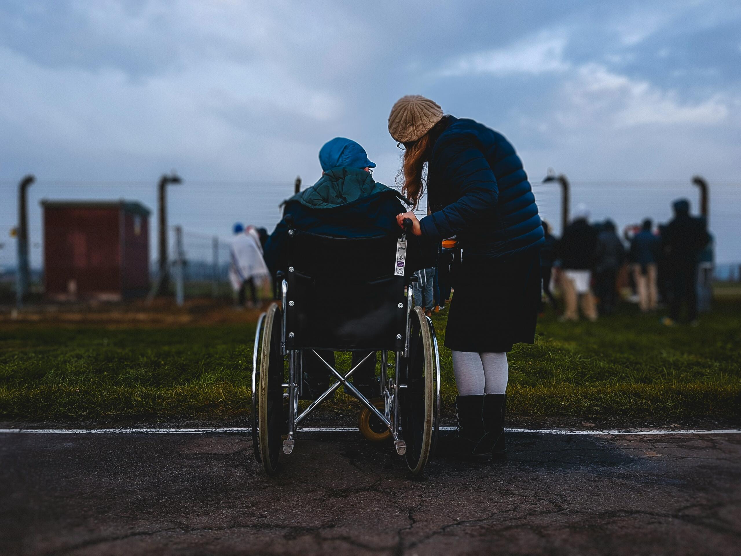 Person in a wheelchair talking to a standing person outdoors at a gathering.