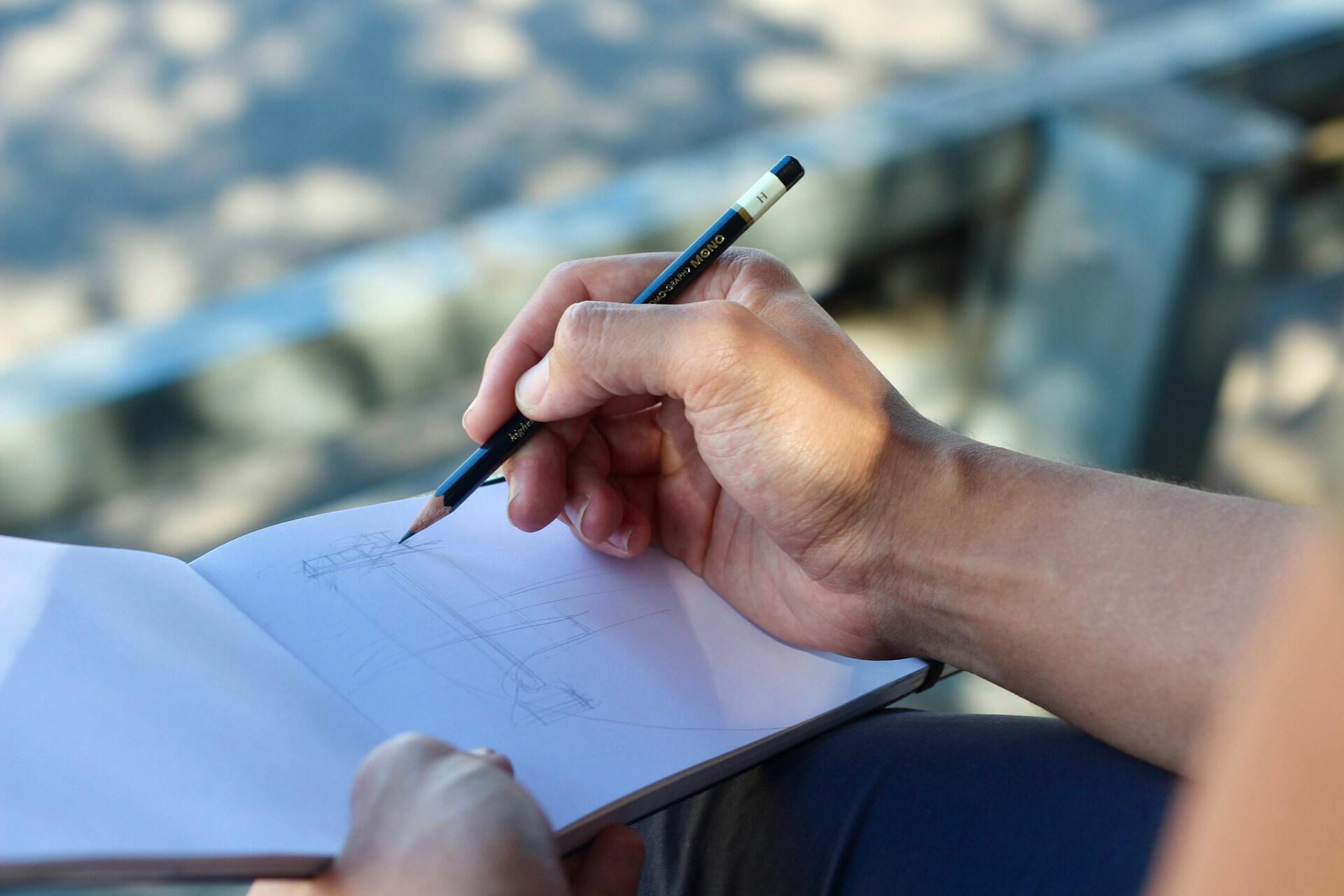 A person sketches outdoors with a pencil.