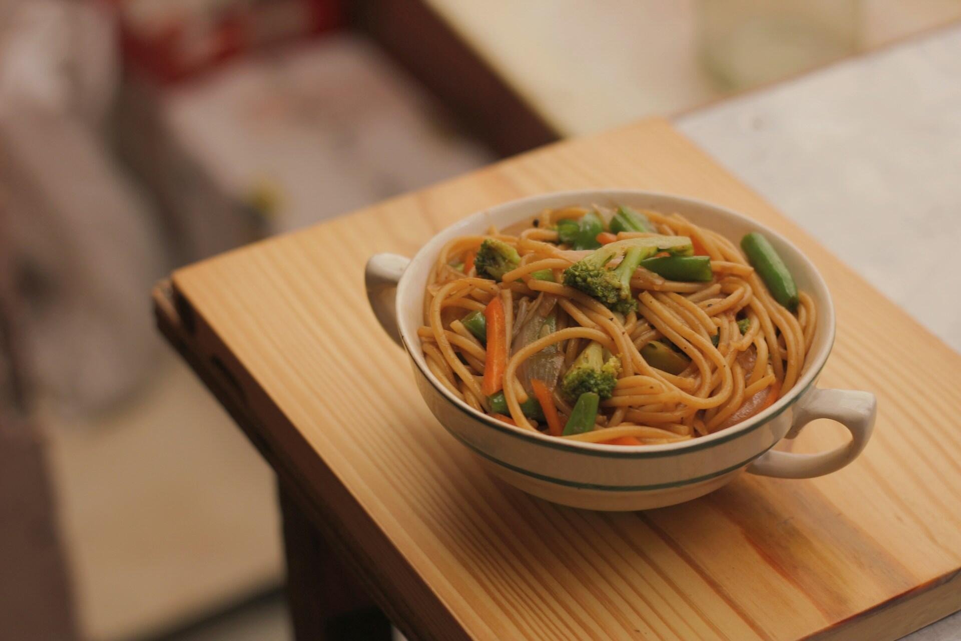 A bowl of Chinese noodles with bits of veg.