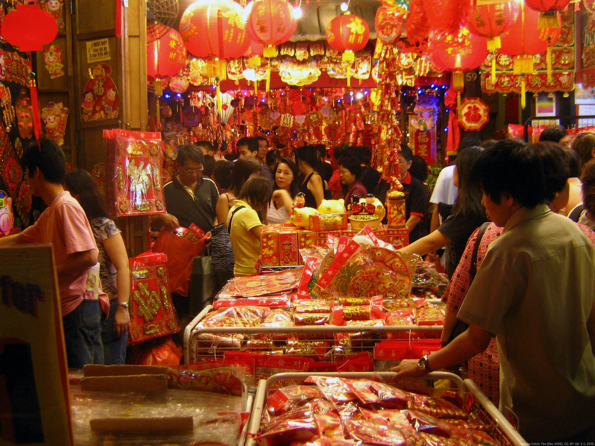 People milling through a Chinese New Year market, the ceiling is covered in red lanterns.