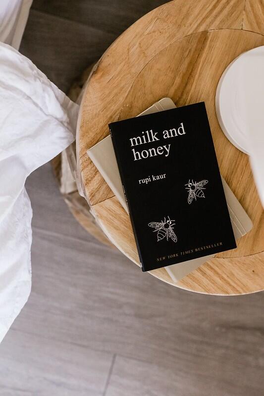 the book -milk and honey on a rounded table beside a bed.