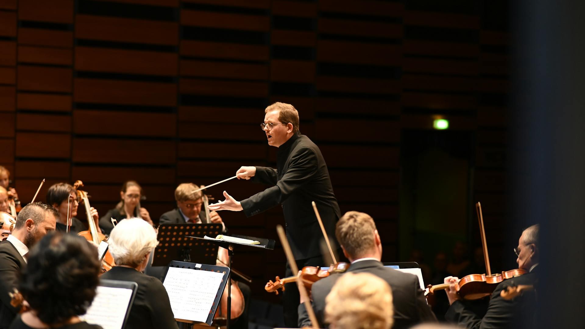 A conductor leads an orchestra including violinists
