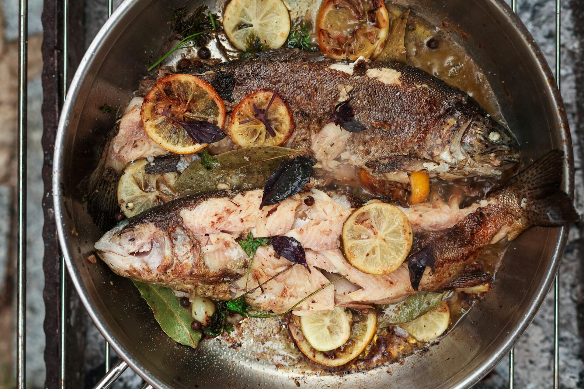 Two whole fish in a frying pan with lemon slices.