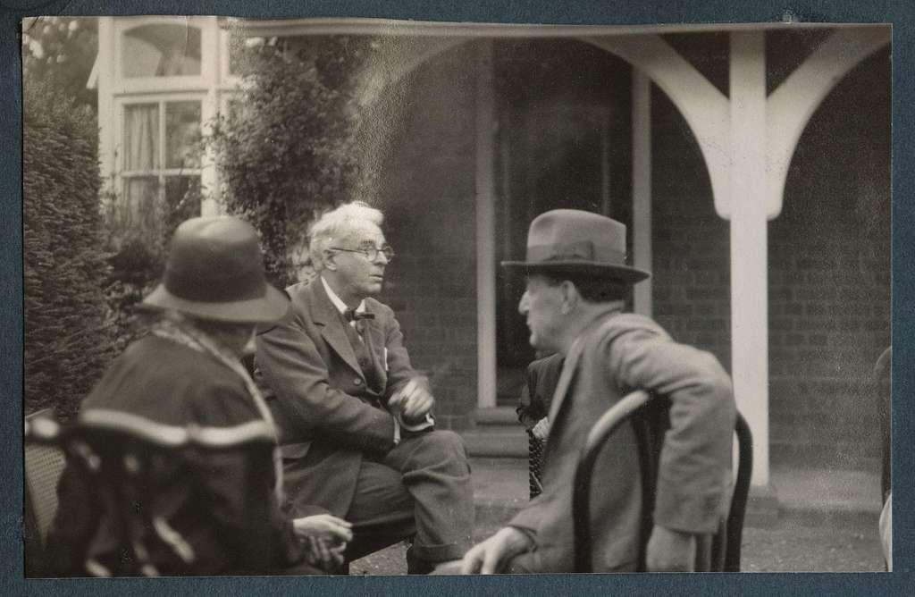 a black and white photograph of modern poets William Butler and Walter de la Mare sitting in front of a house