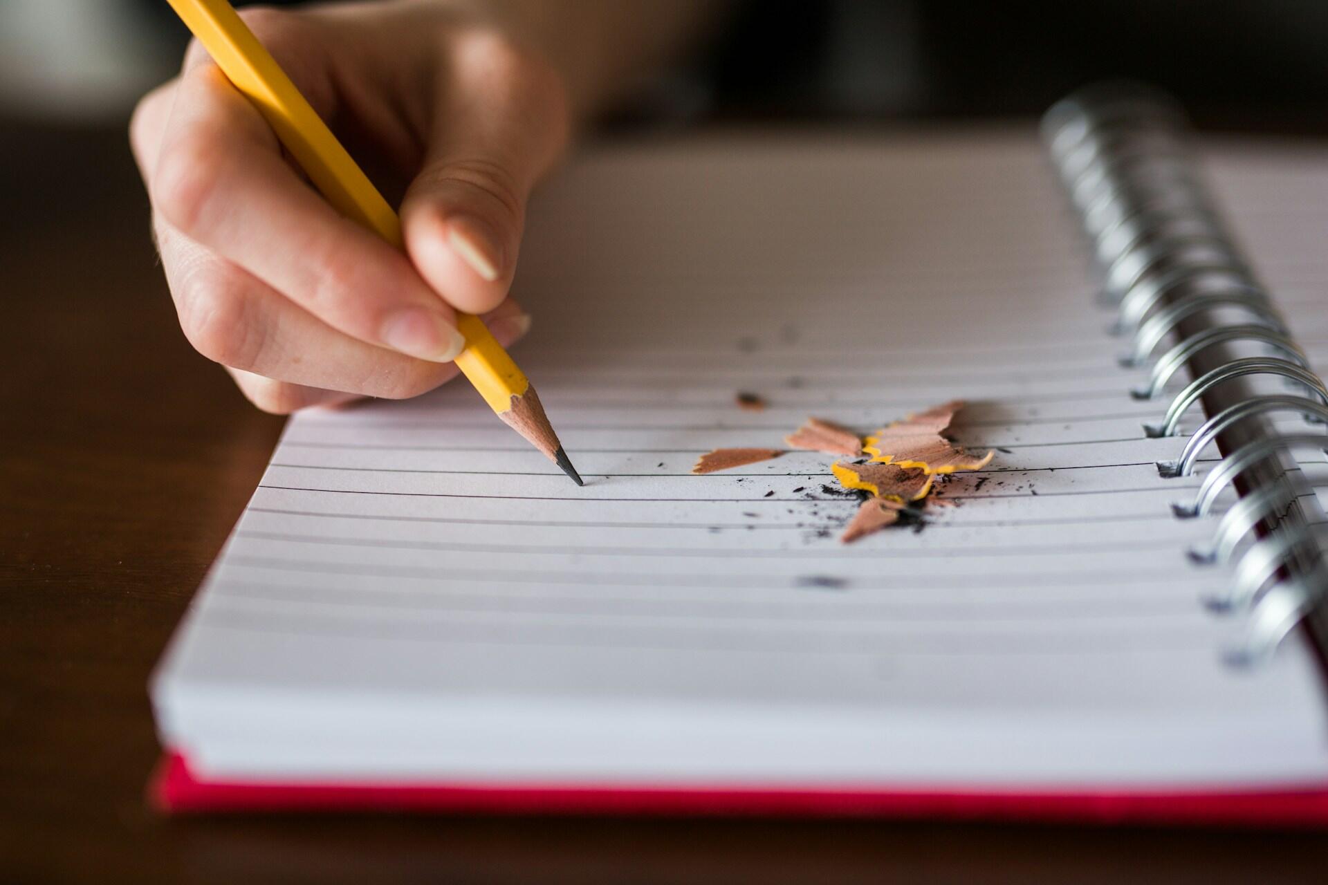 A person writing with a pencil in a notepad.