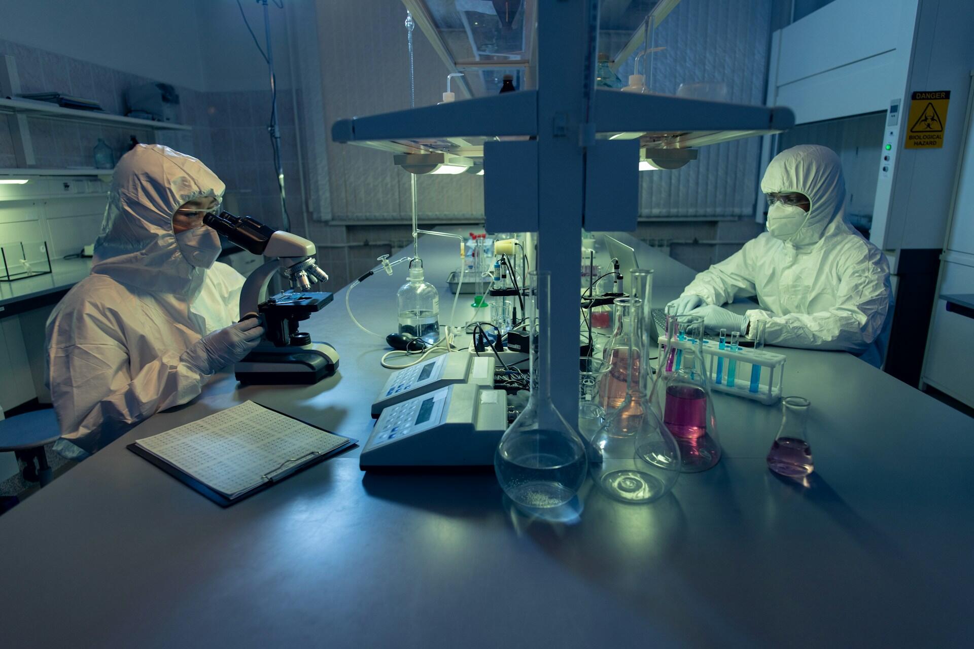 Two people wearing safety gear at a laboratory workbench. 