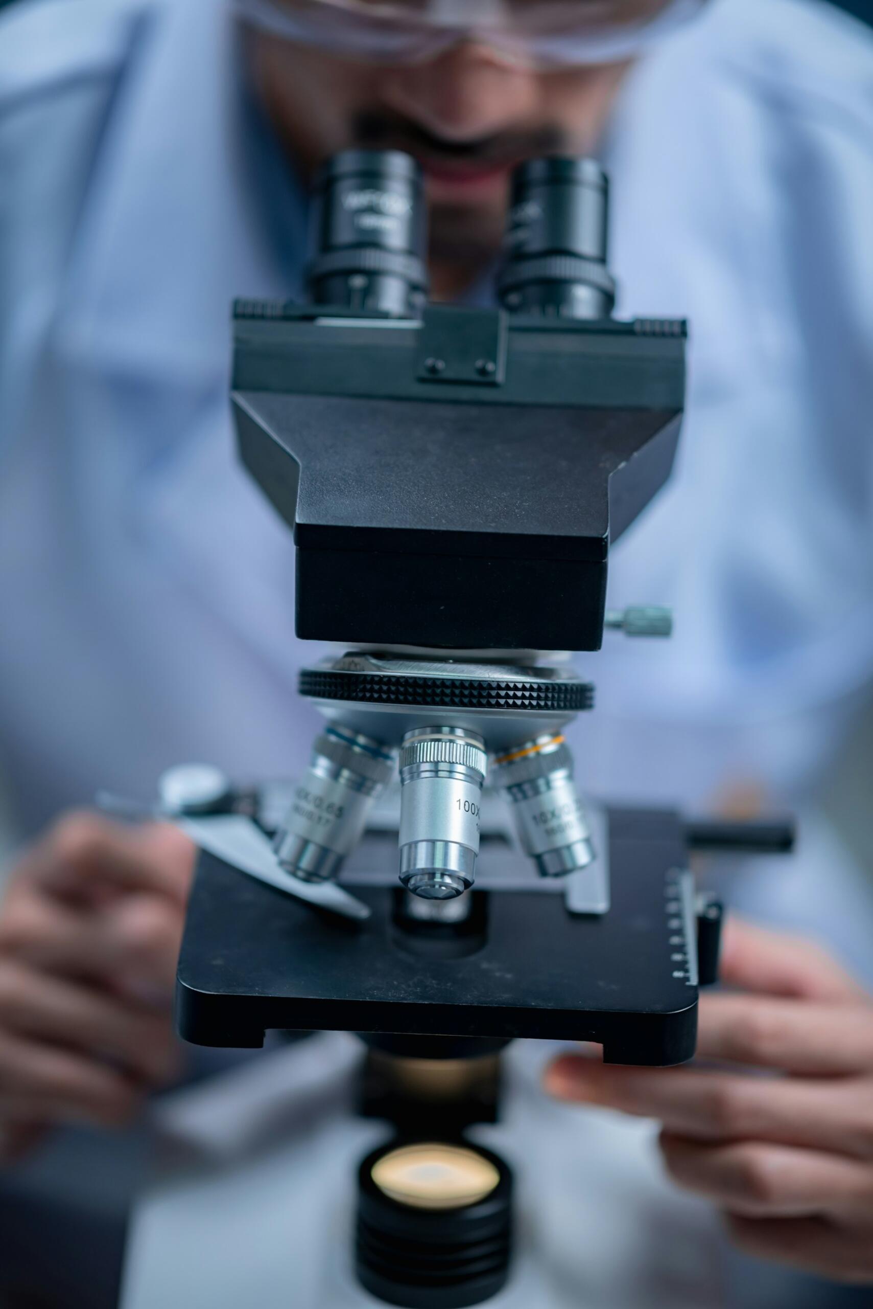 A bearded man peers into a microscope.