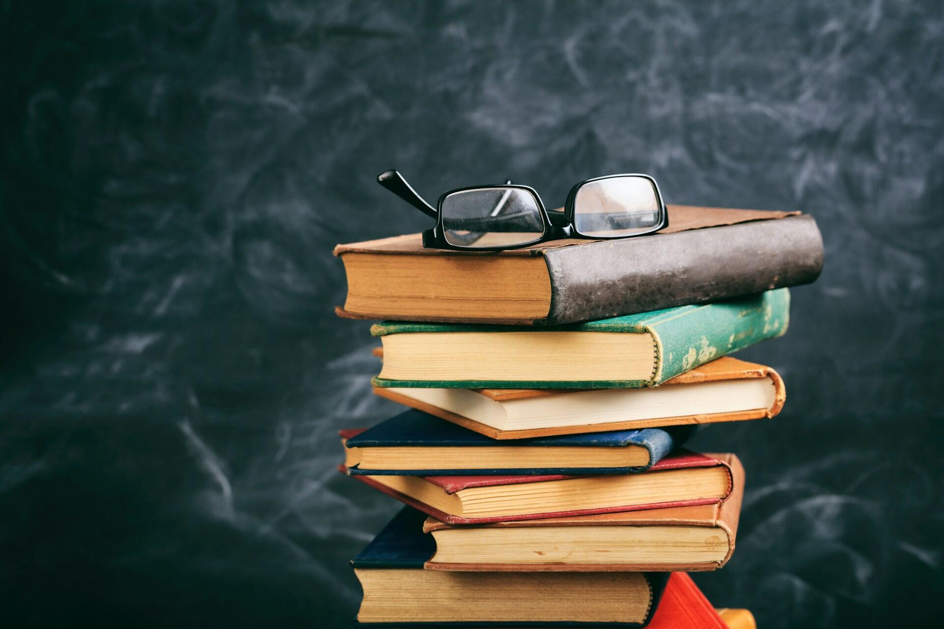 pile of school textbooks with reading glasses on top