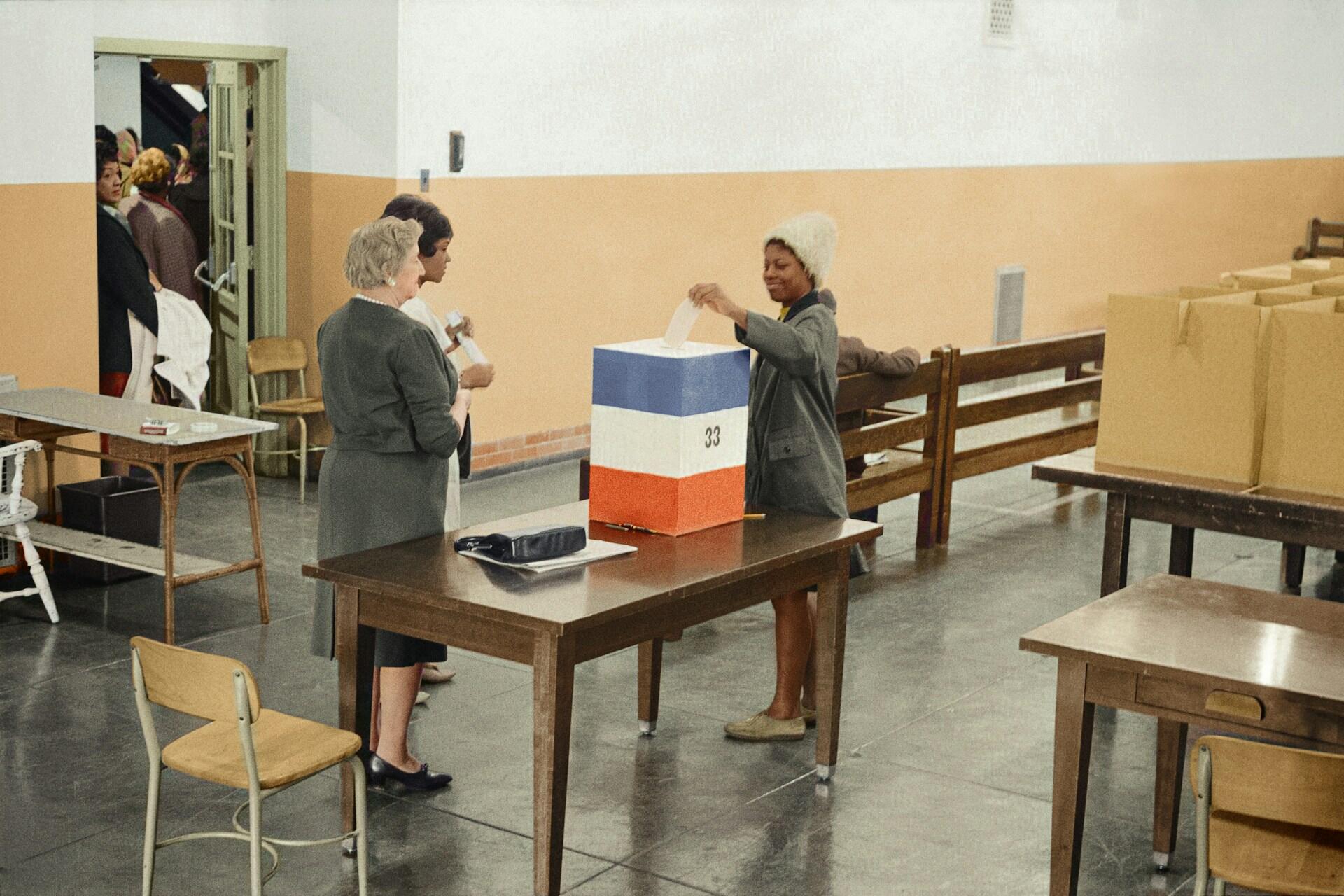 People standing next to a tricoloured box in an empty room. 