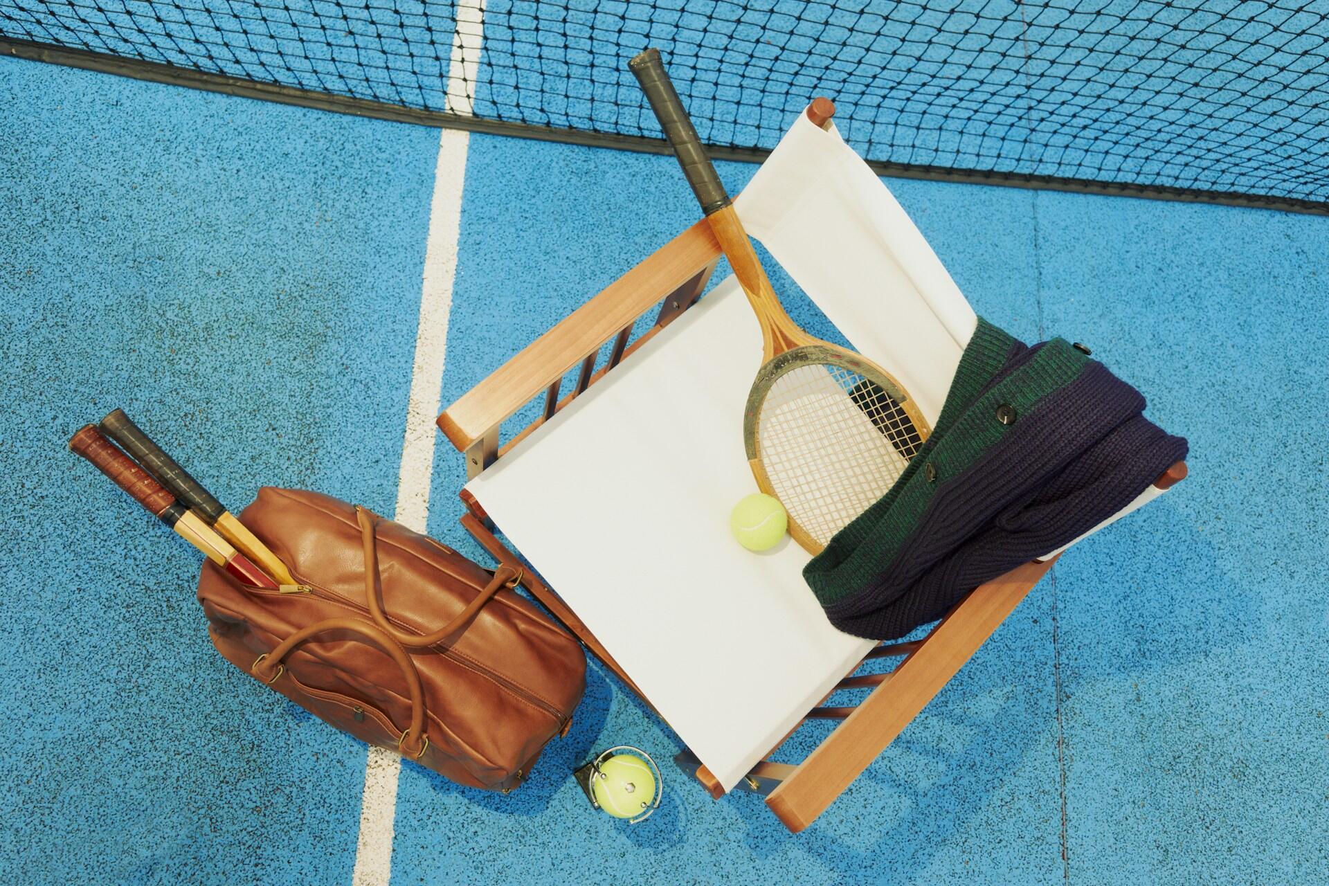 A bag with tennis equipment next to a chair on a tennis court.