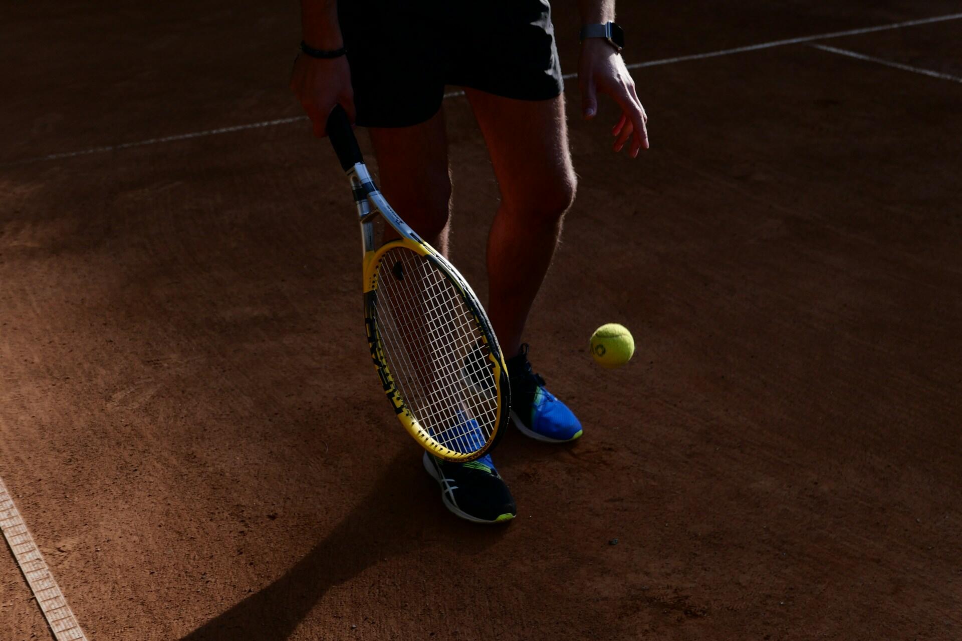A tennis player on a clay court in shadow.