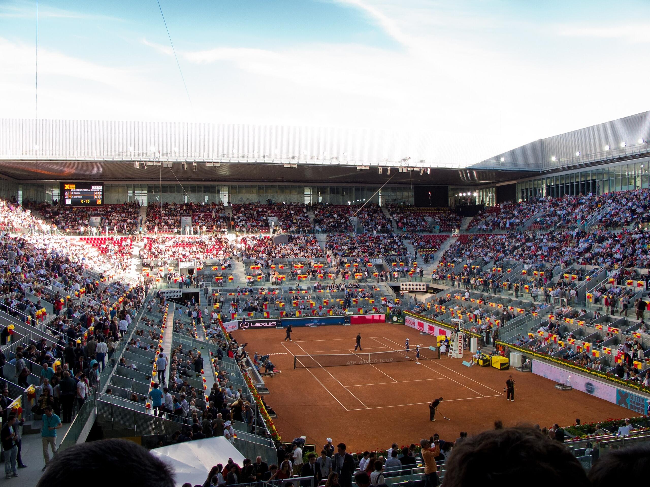 A tennis venue with roof retracted and spectators watching on a sunny day. 