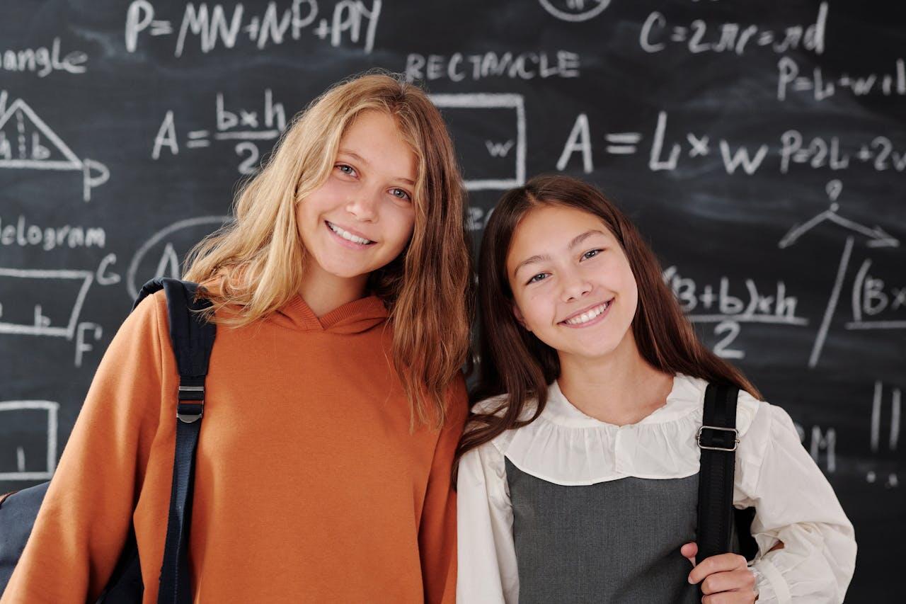 two female students standing in front of a blackboard filled with math equations
