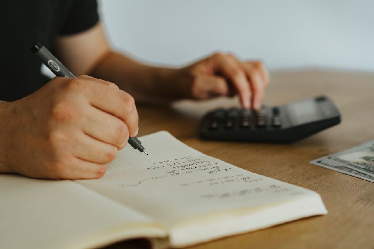 someone writing down calculations in a notebook while using a calculator