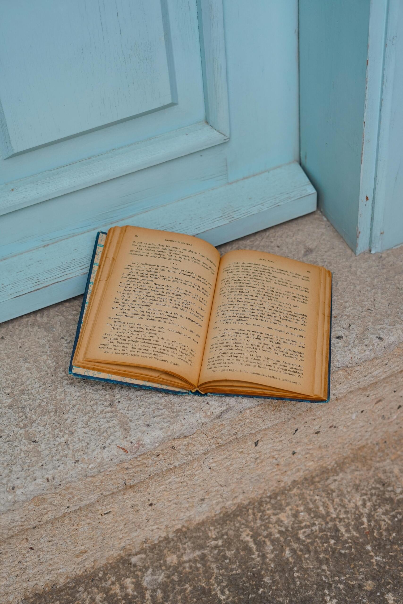 An open vintage book with yellowed pages resting on a rustic wooden floor.
