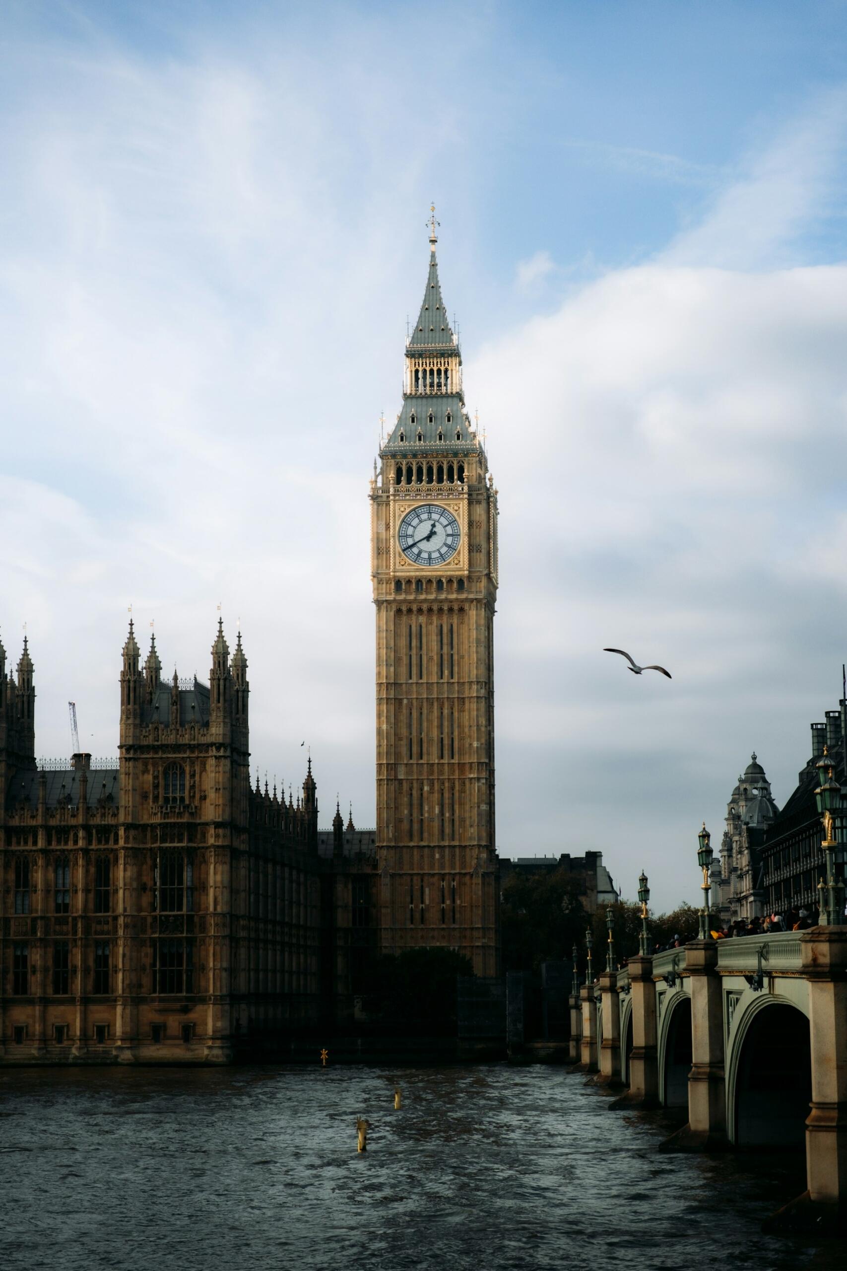 A tall stone tower with a clock at its top overlooking a river.