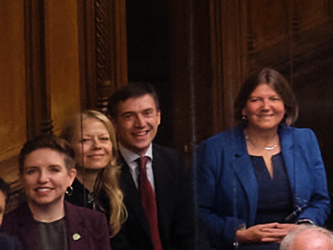 Four people in business dress, in a formal chamber. 