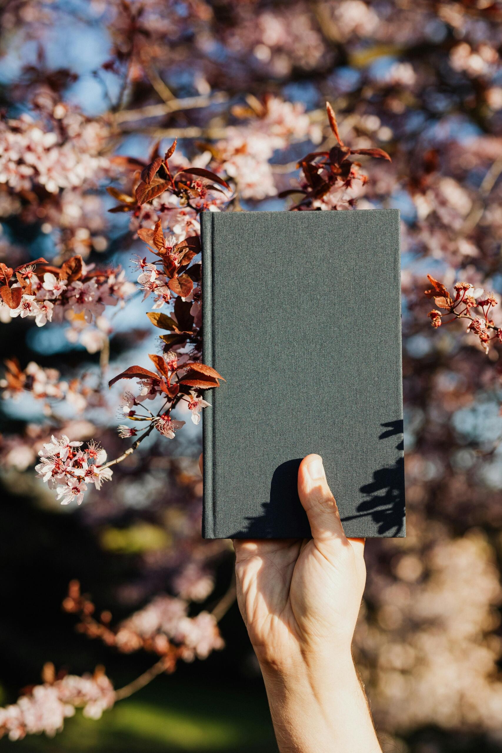  A person holding a black notebook while sitting in a blooming garden filled with vibrant flowers.