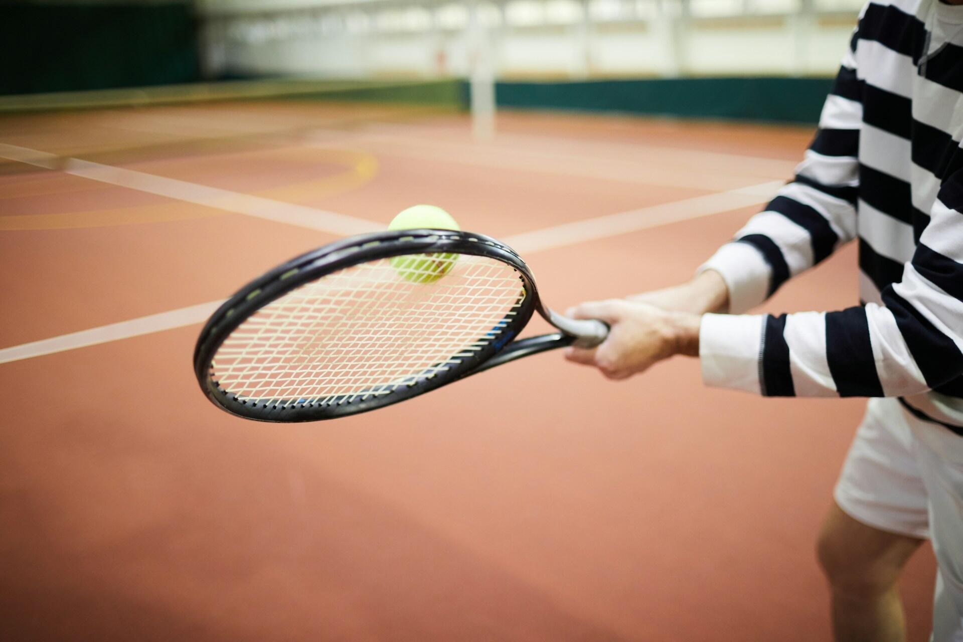 A tennis player in a striped shirt hits the ball.