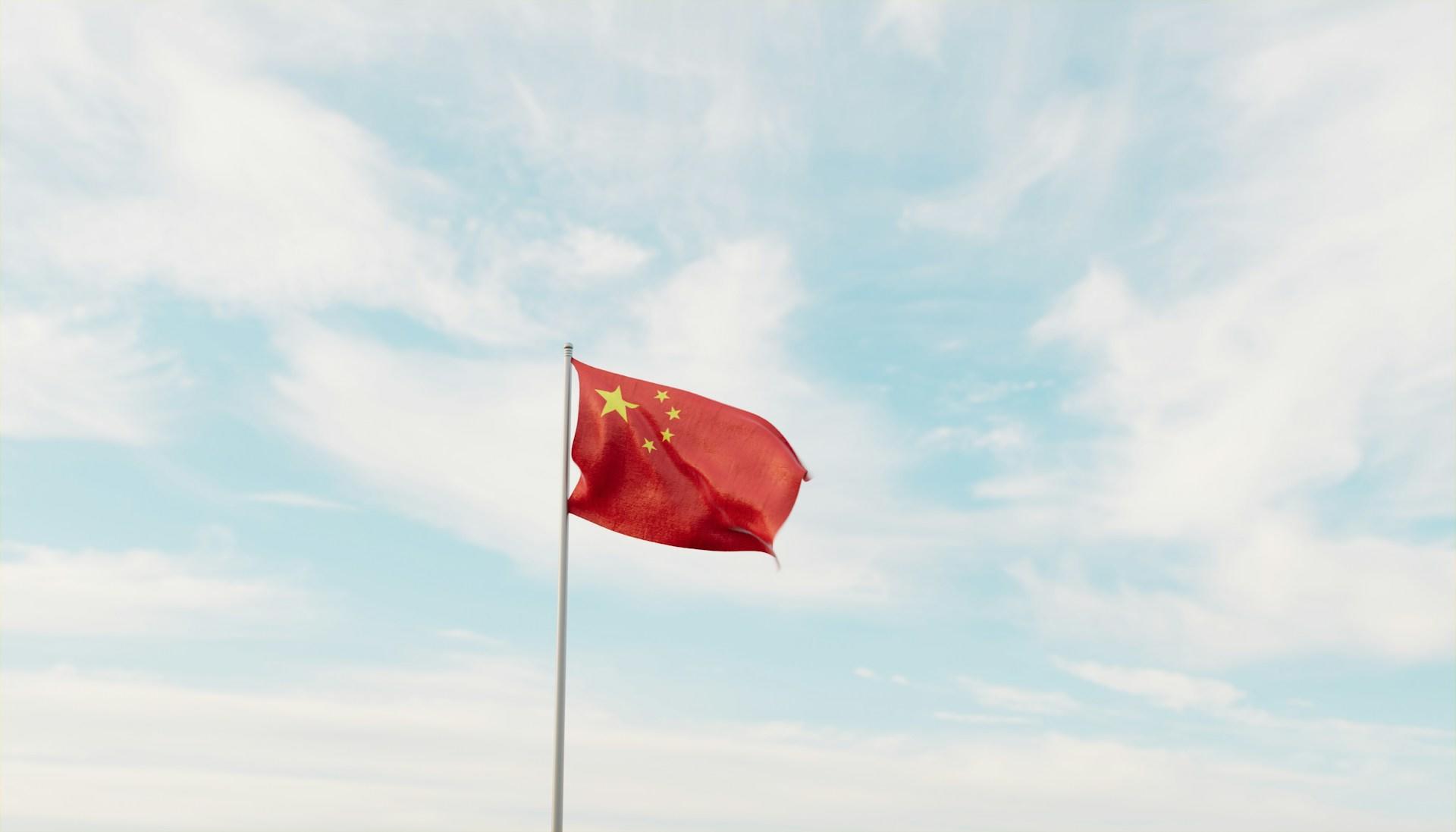 A Chinese flag fluttering in a blue sky with diffuse clouds.