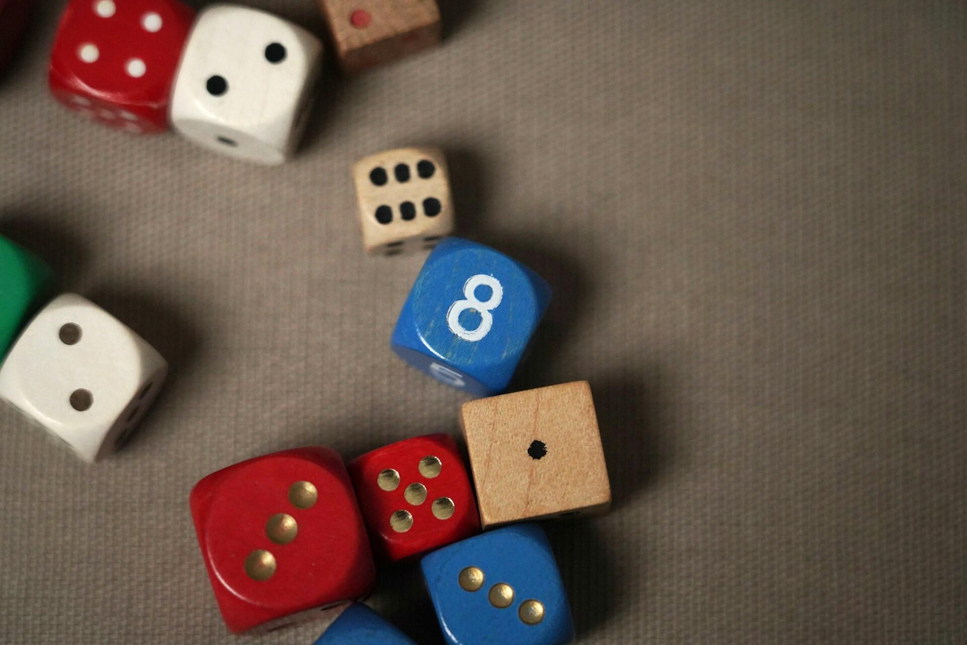 A collection of colorful dice scattered on a textured surface, including a prominent blue die showing the number 8.