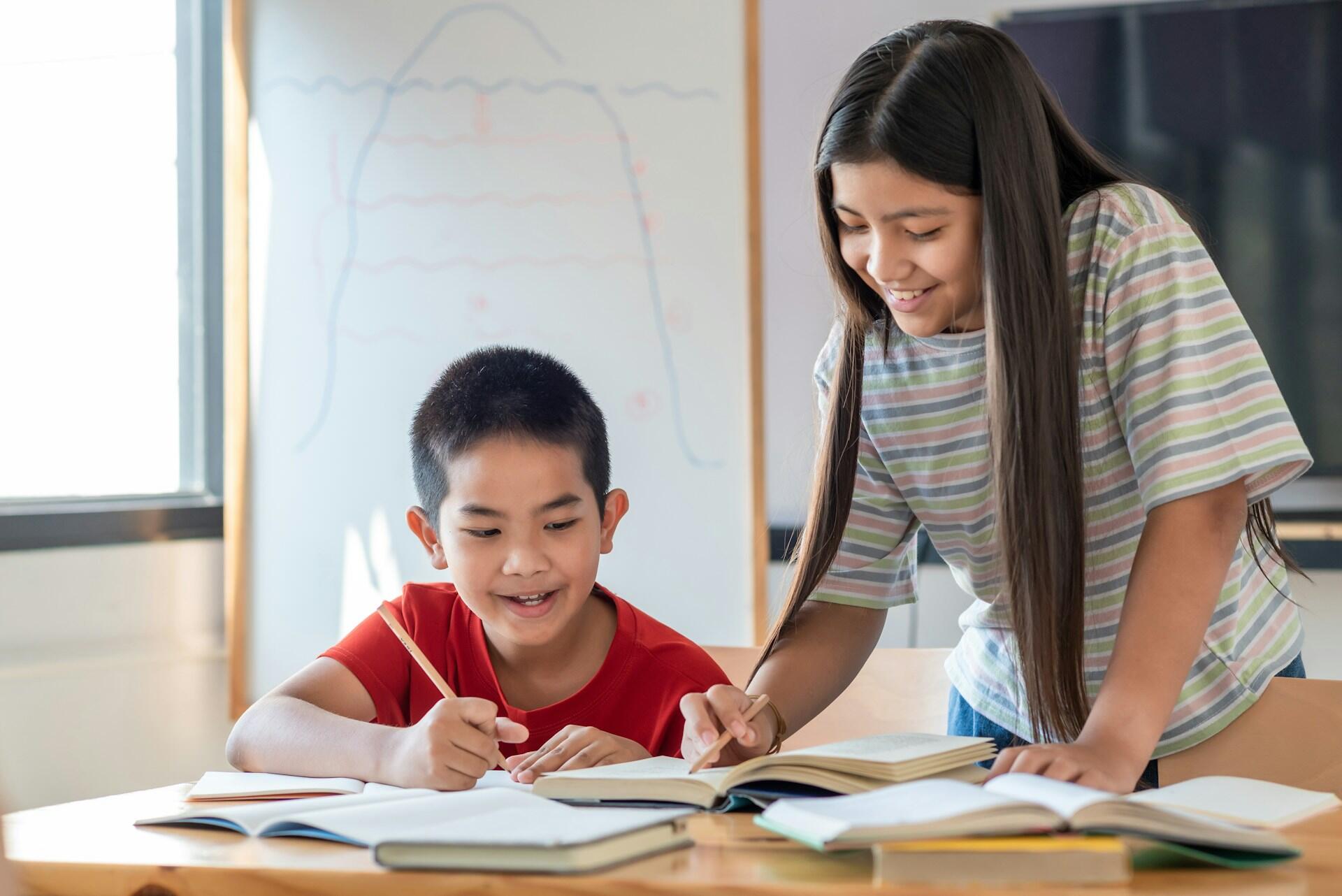 young boy and girl working at a desk with a pile of books