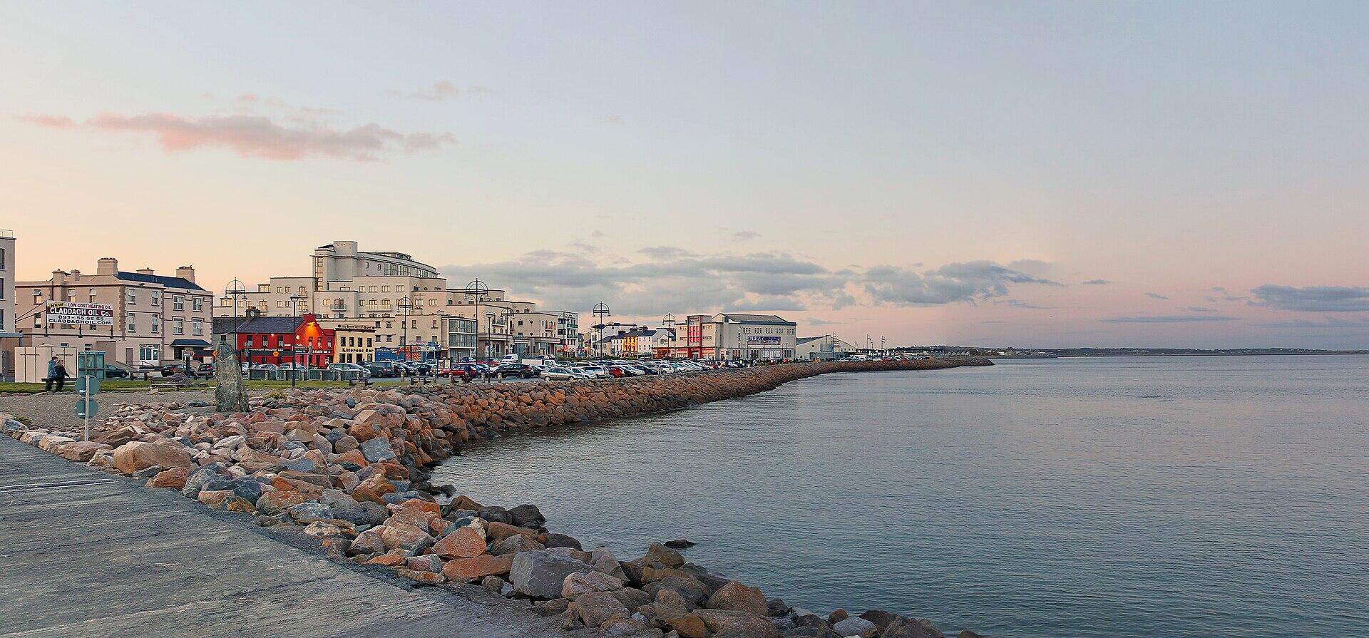 A walkway next to the water, with a city in the background.