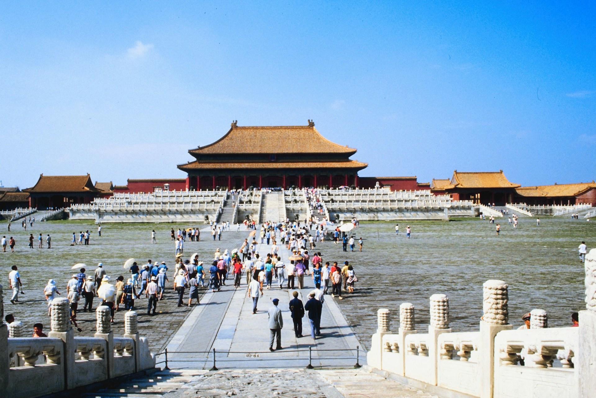 Visitors in Beijing's Forbidden City, featuring historic architecture under a blue sky.