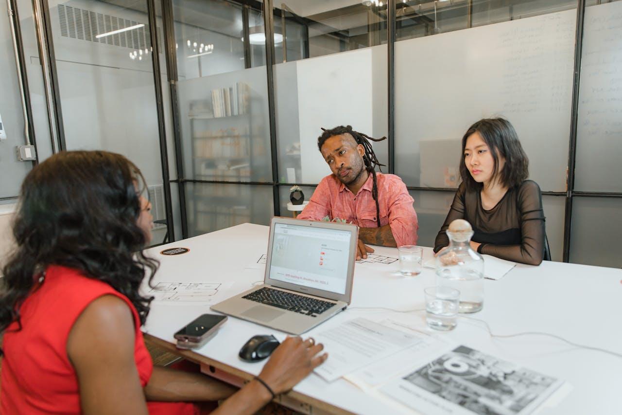 A group meeting at a modern conference table, featuring laptops, water glasses, and design documents in a stylish office space.