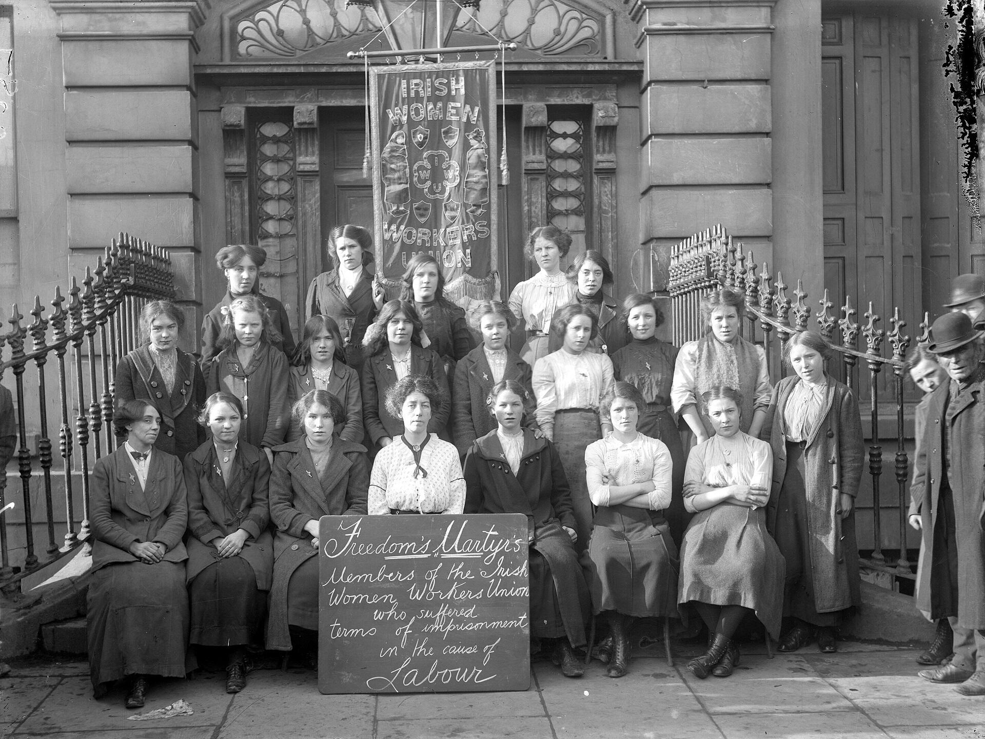 A group of women posing on the steps of a building, with a sign in front of them.