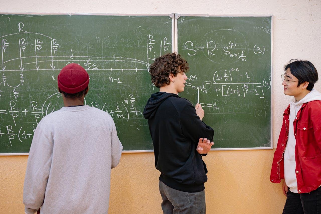 Three students discussing complex mathematical equations on a green chalkboard, with various formulas and graphs visible.