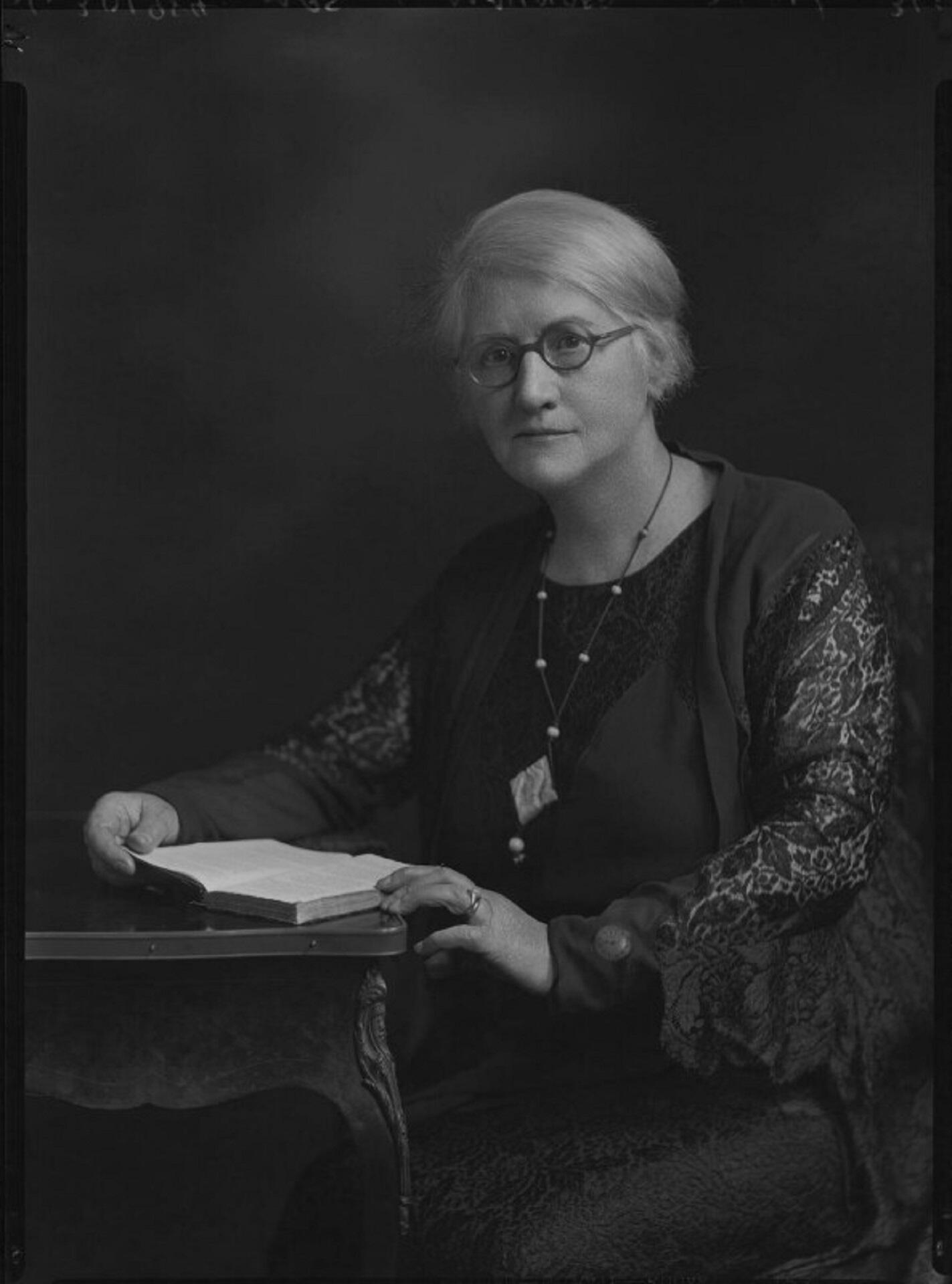 A woman wearing glasses, seated at a table.