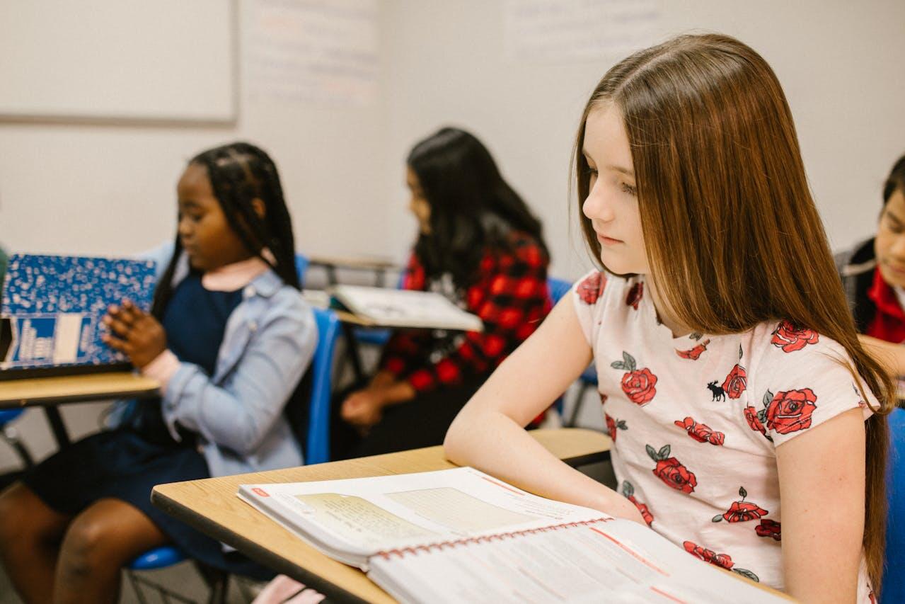 A group of students sits at desks in a classroom, focused on their textbooks and notebooks, engaged in learning activities.
