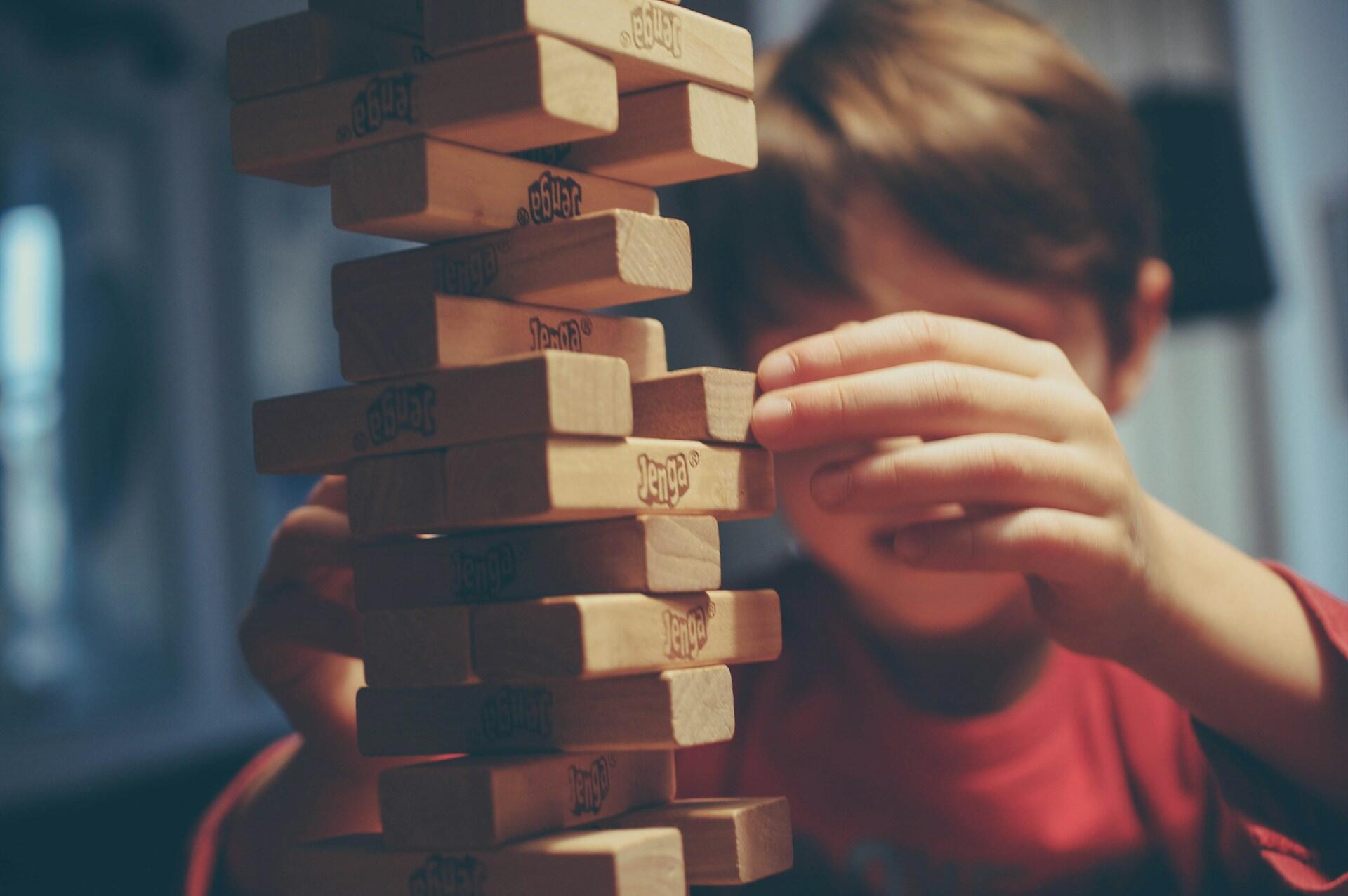 A child in a red shirt carefully removes a Jenga block from a tall tower, focusing intently on the game.