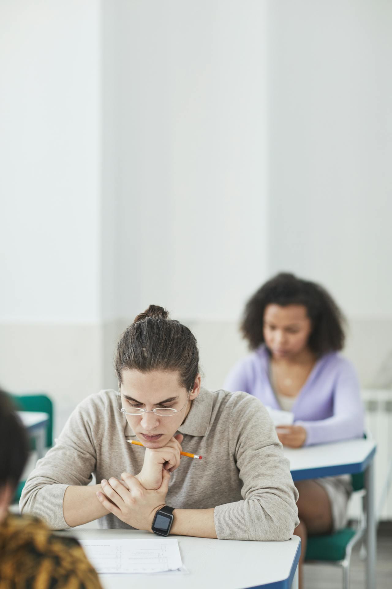 Students seated at desks during an exam, focused on their papers in a bright classroom setting.