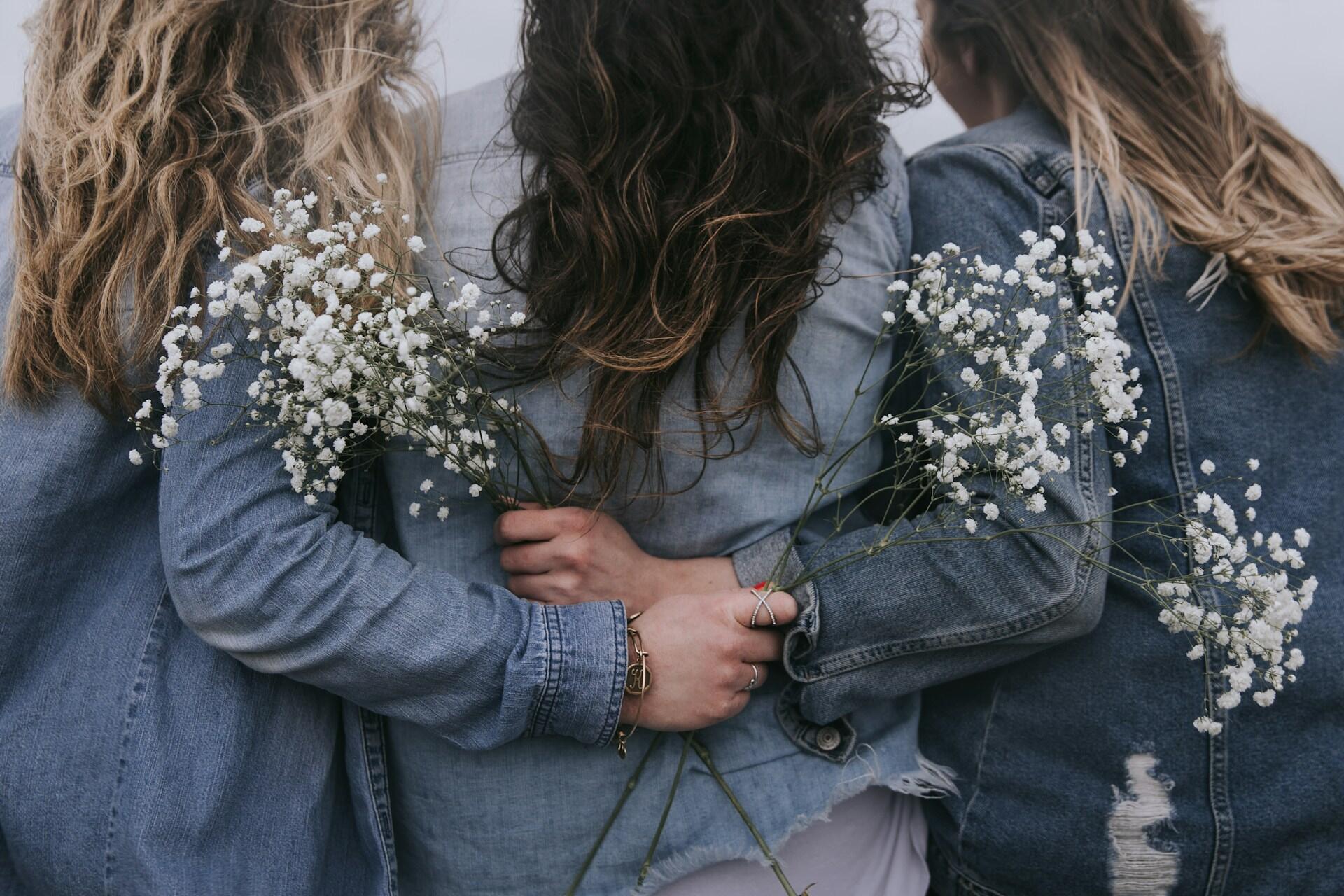 Three women in denim jackets carrying flowers.