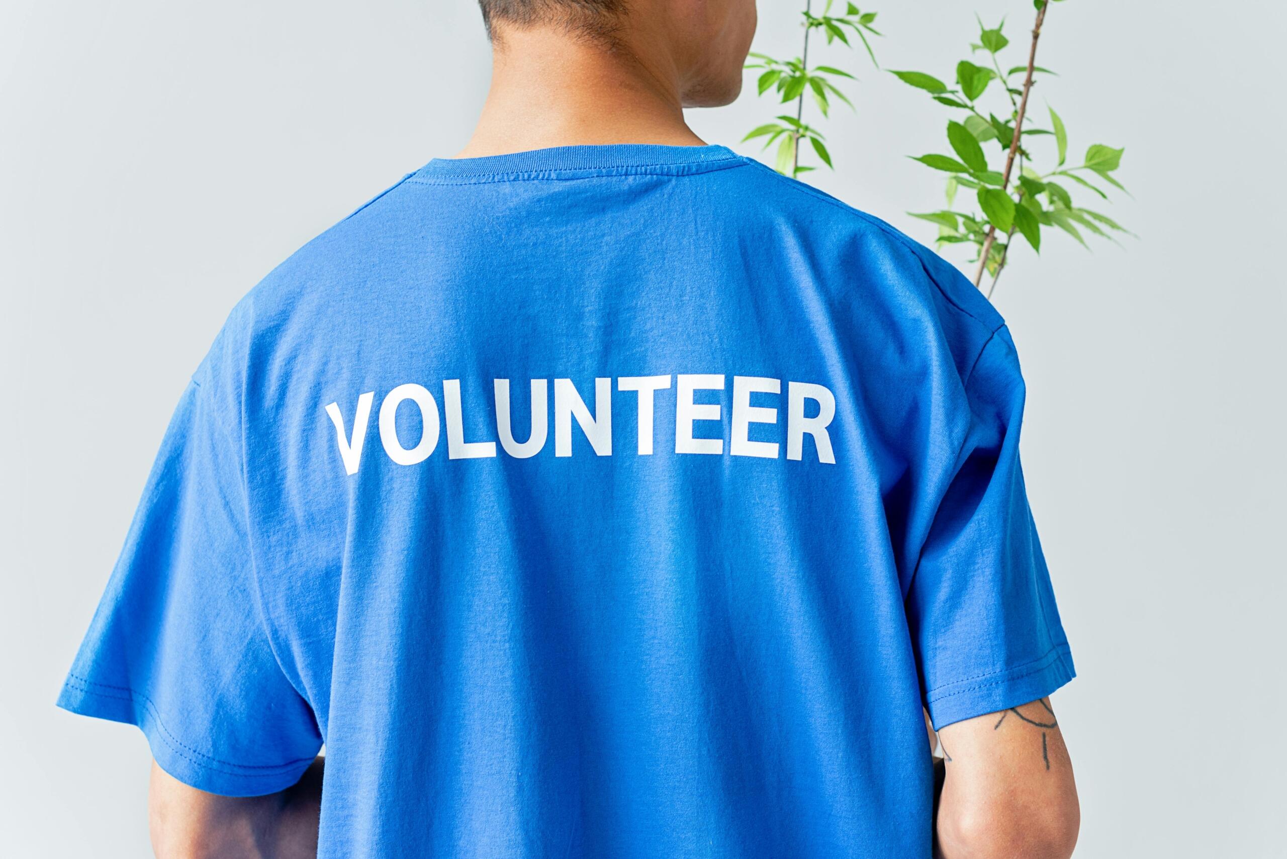 Close-up of a man wearing a blue shirt with the word “VOLUNTEER” printed in bold white letters on the back.