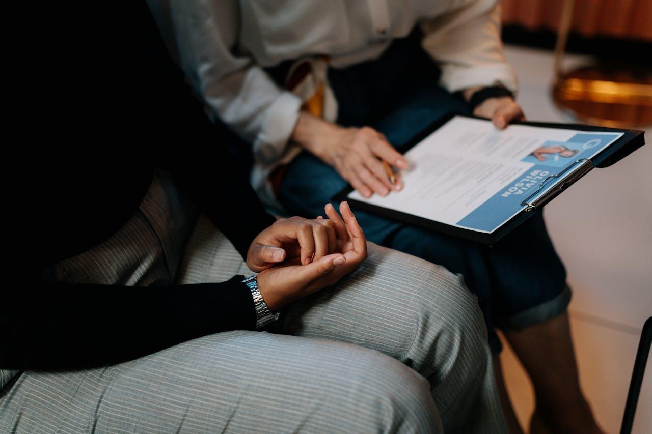 Two people sit close together, one holding a clipboard with a document, while the other rests their hand in contemplation.