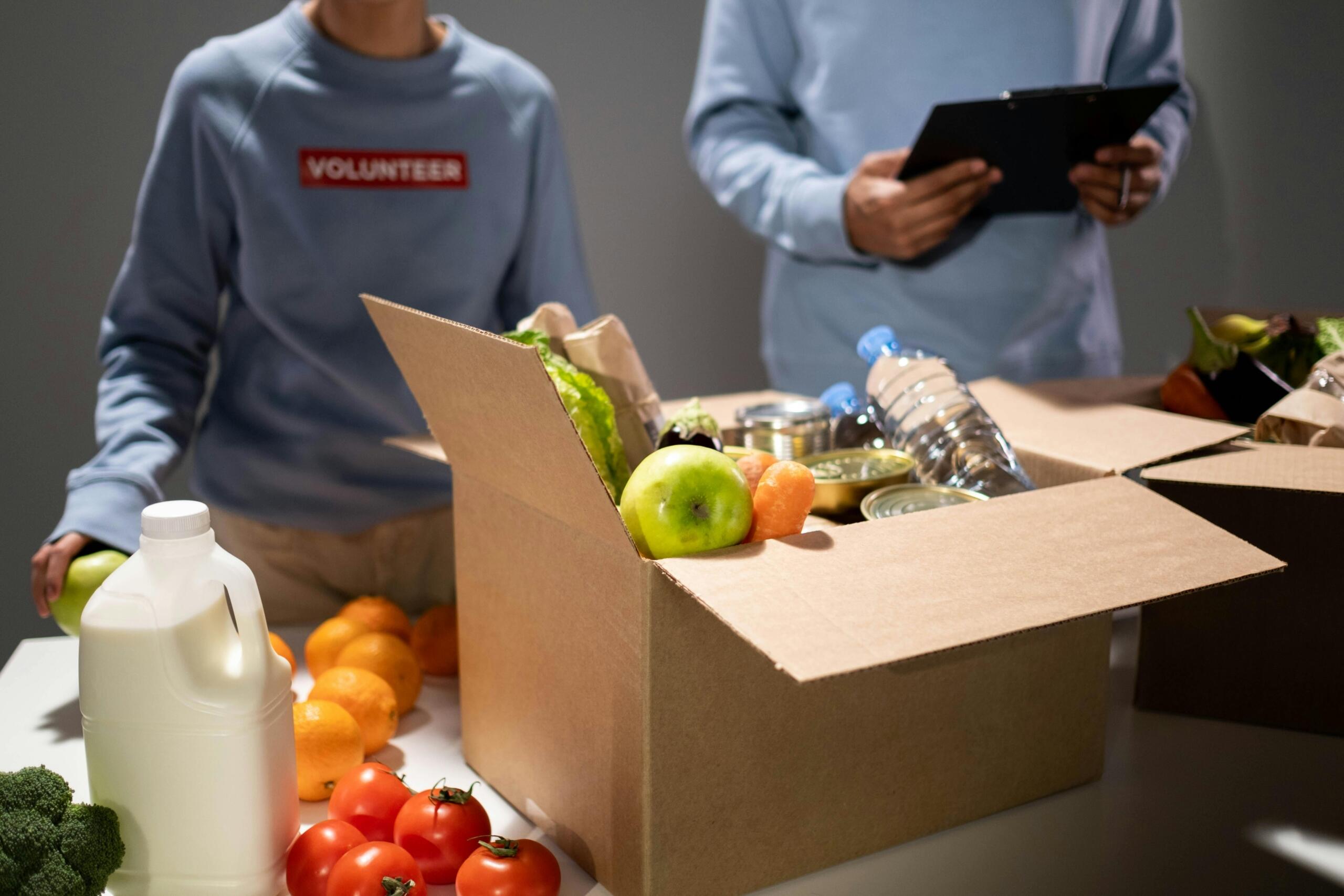 Assorted food and drink items neatly arranged inside an open cardboard box during a volunteer drive.