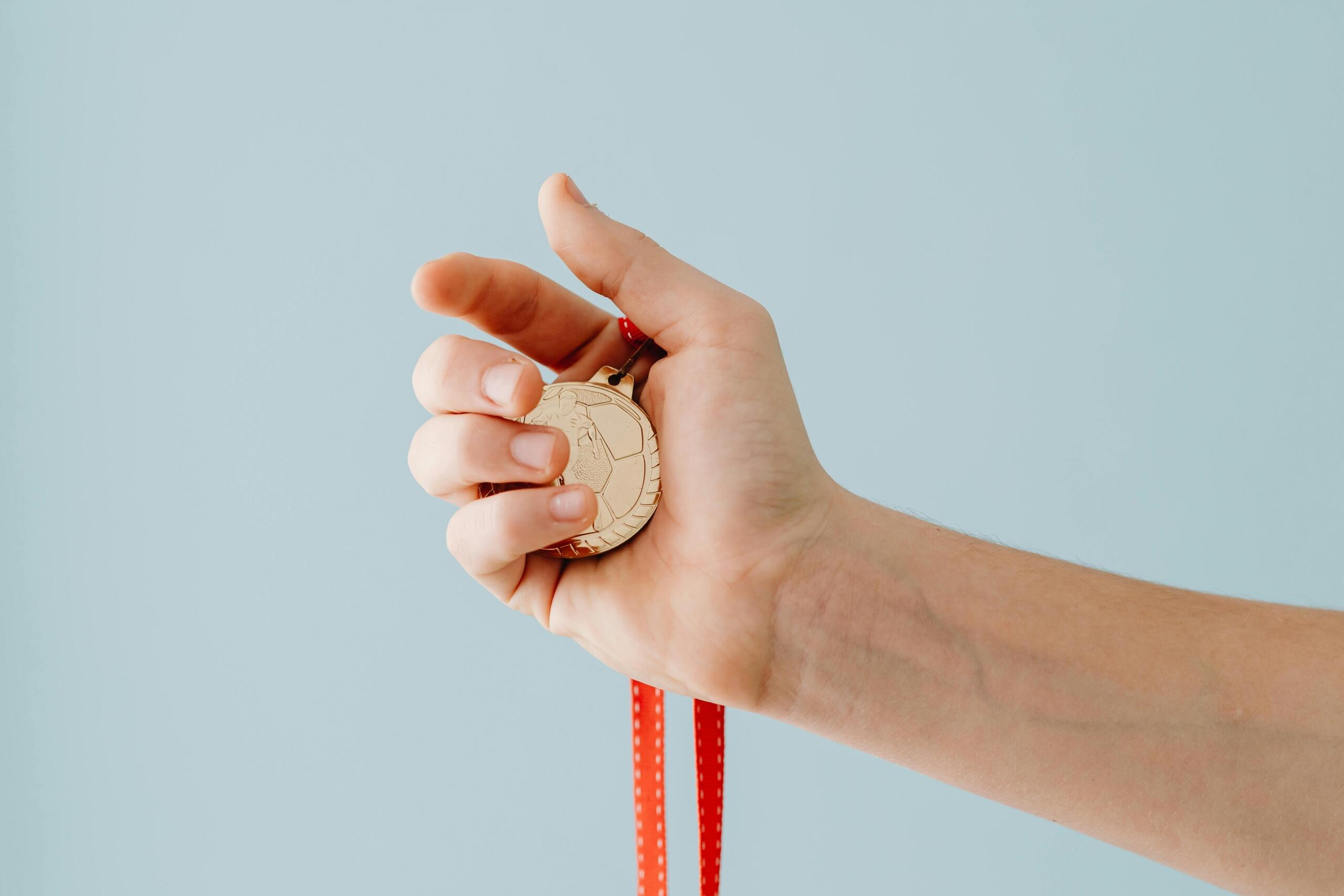 Close-up of a hand holding a gold medal with a ribbon.