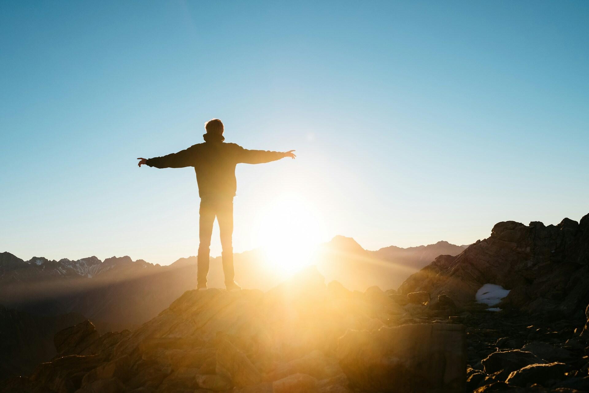 A person with arms spread out on a mountaintop at sunrise.