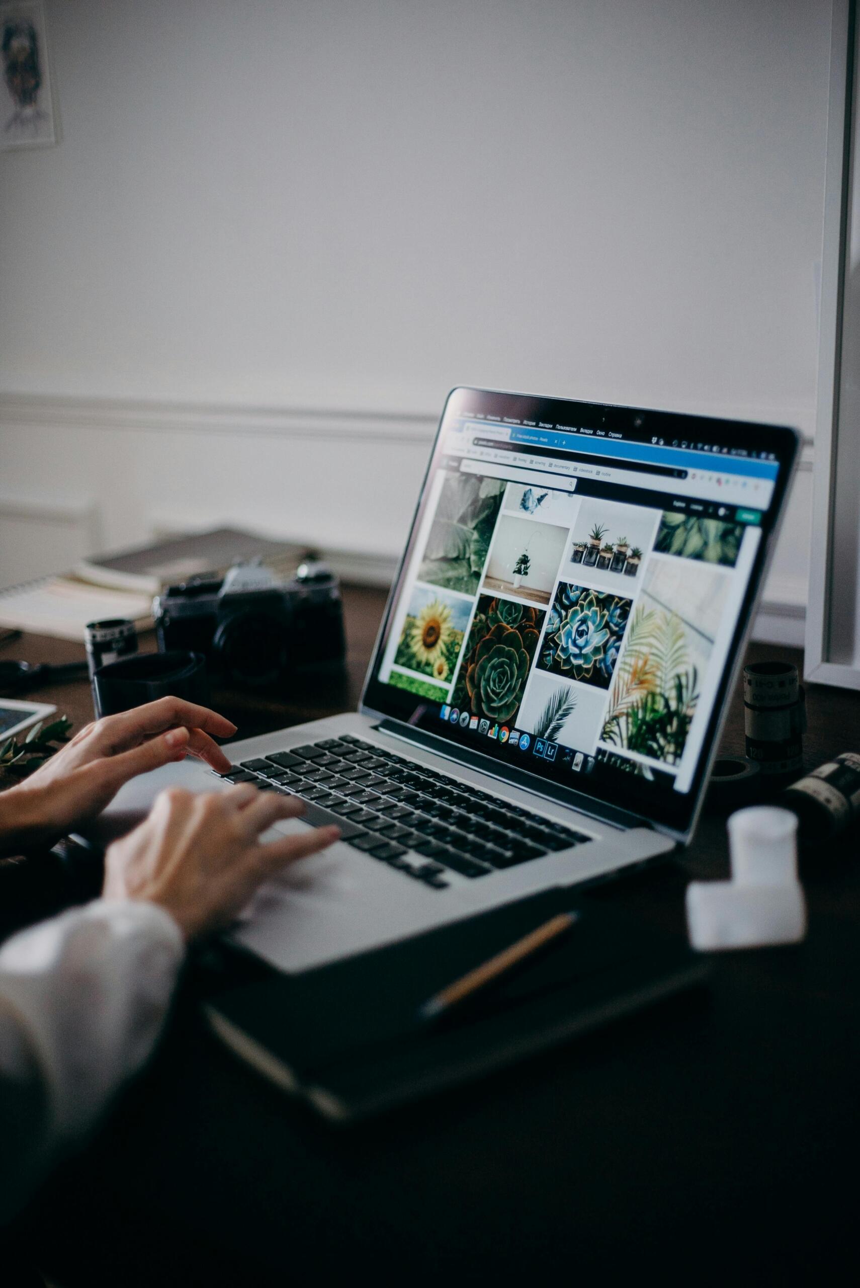 Person working on a MacBook Pro at a table, engaged in graphic or design work.