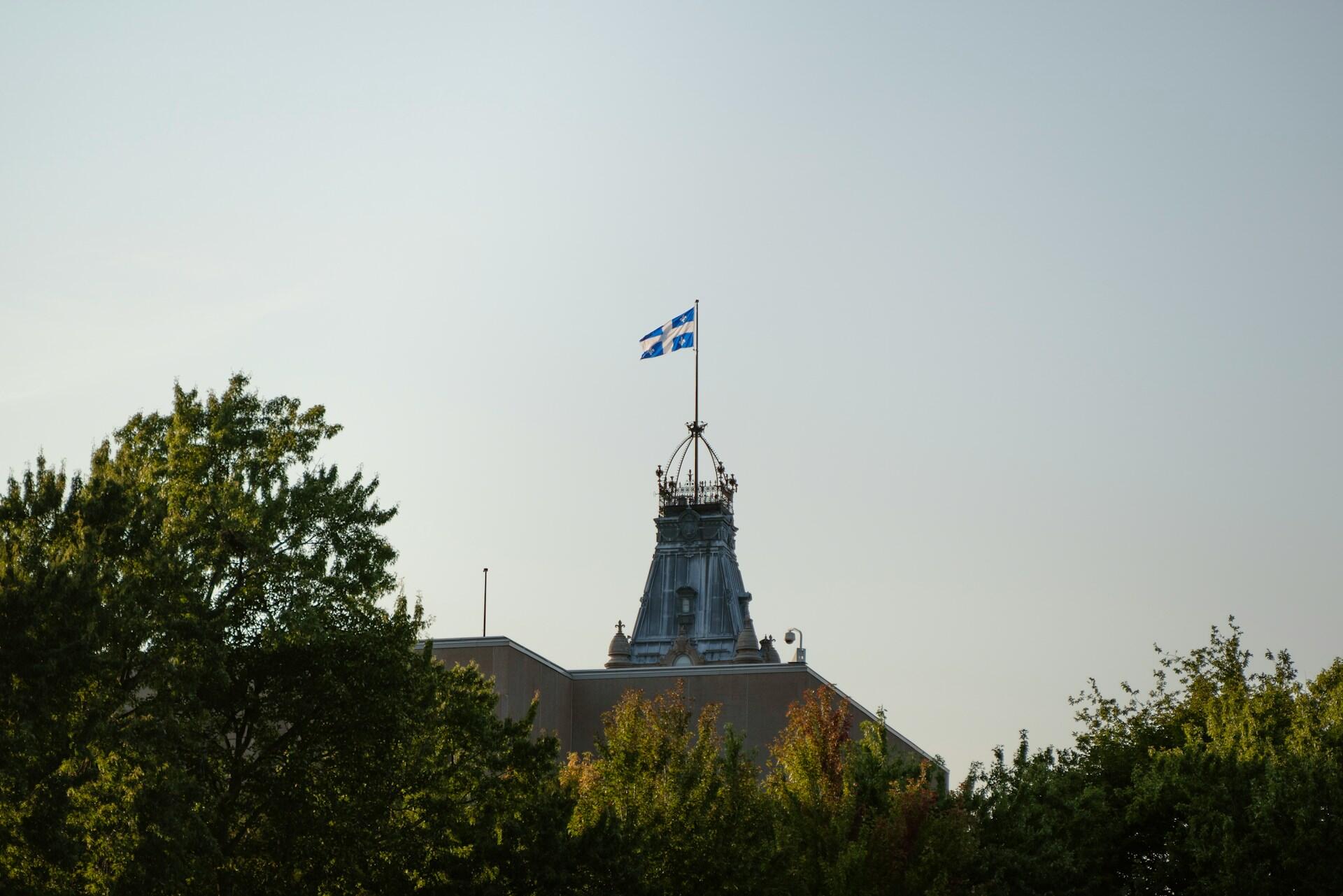 a building with trees in front of it, with a quebec flag on top of the building